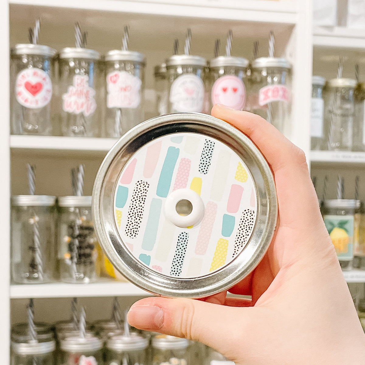 Hand holding mason jar patterned straw lid that has pastel strips on white background 