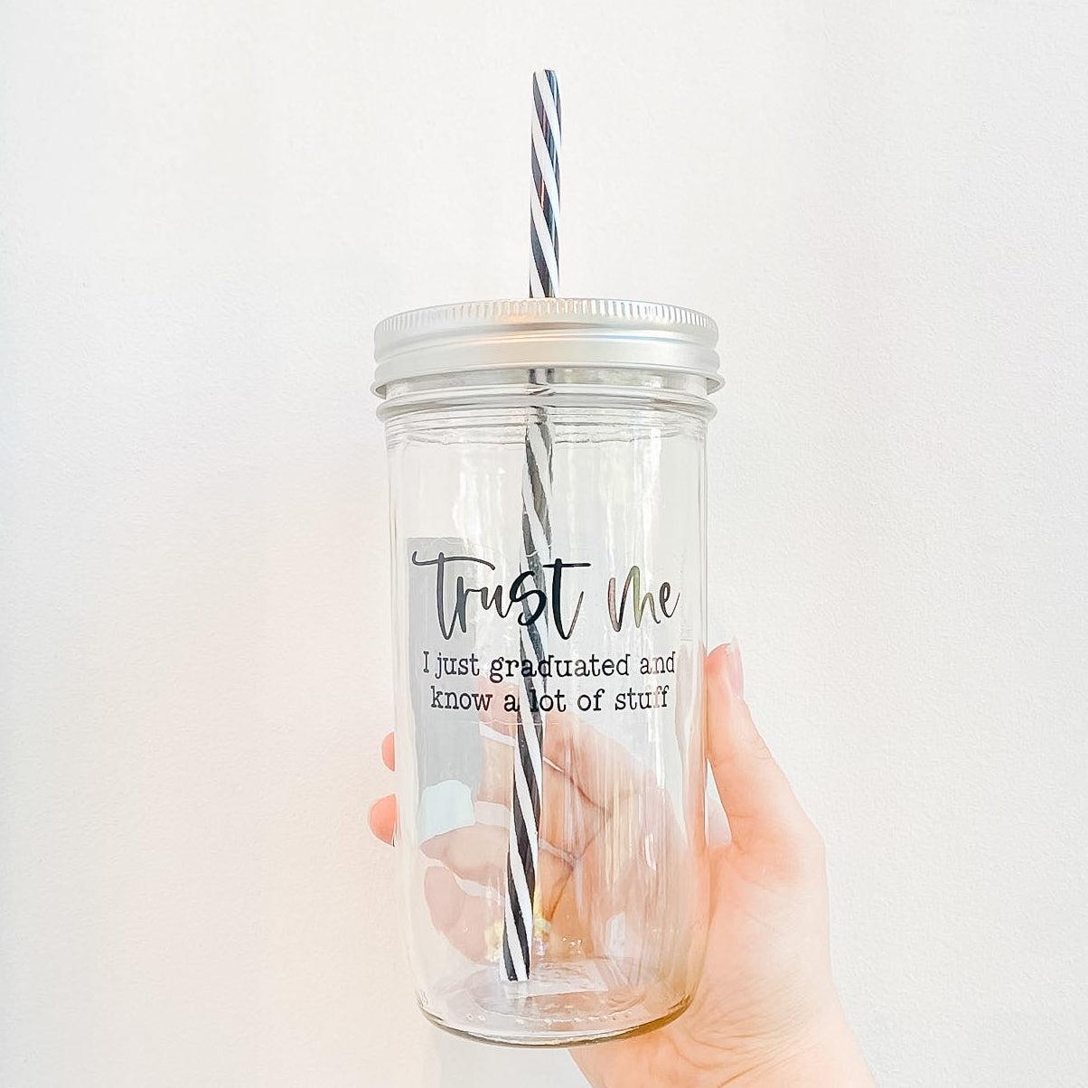 Glass mason jar tumbler with “Trust Me, I Just Graduated and Know a Lot of Stuff” design, reusable striped straw, and patterned mason jar style lid.
