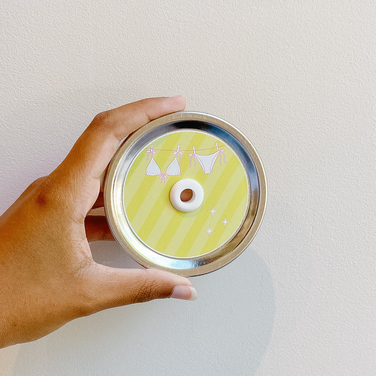 Hand holding mason jar patterned straw lid that is yellow striped with a pink and white bikini design