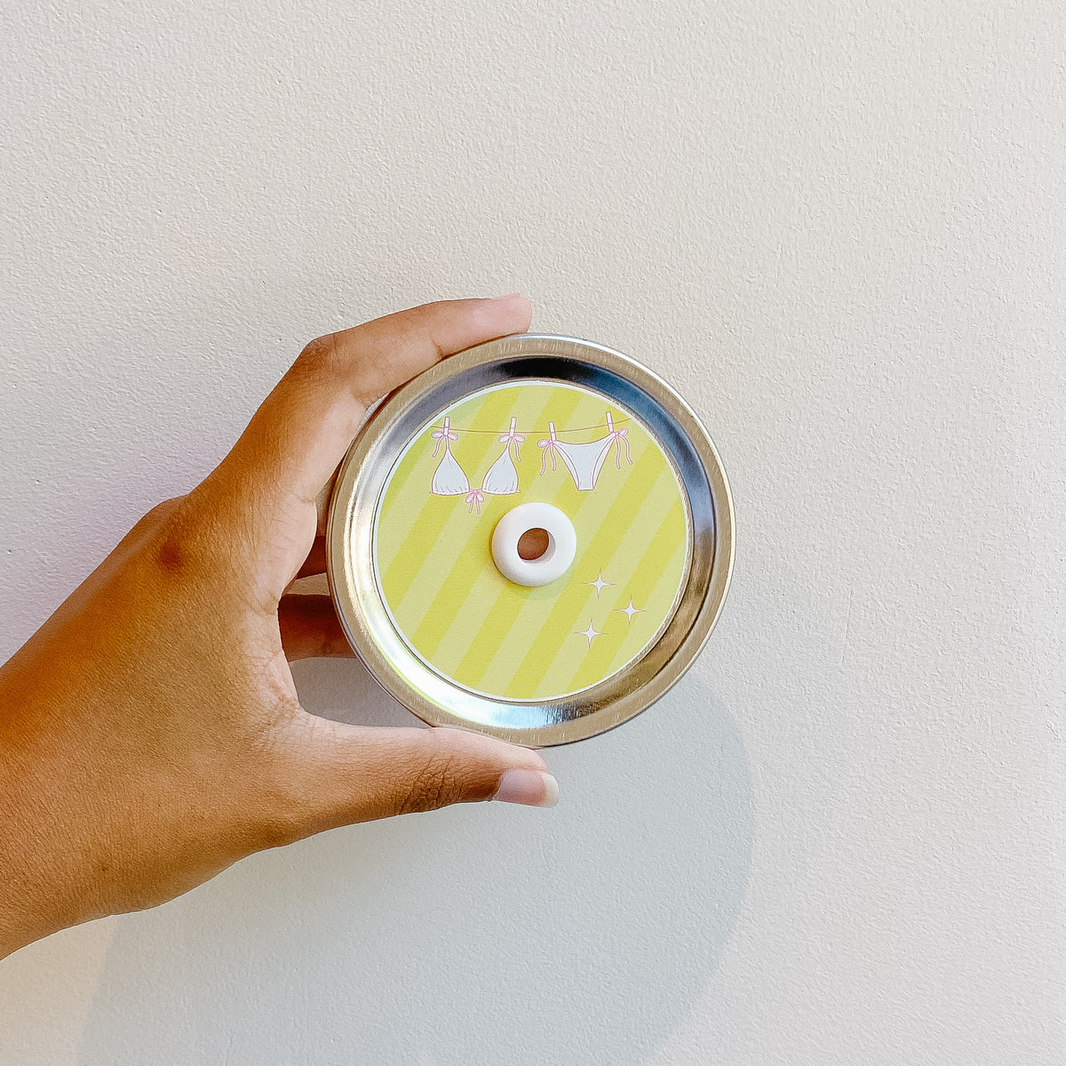 Hand holding mason jar patterned straw lid that has pink outlined bikini design on yellow striped background 