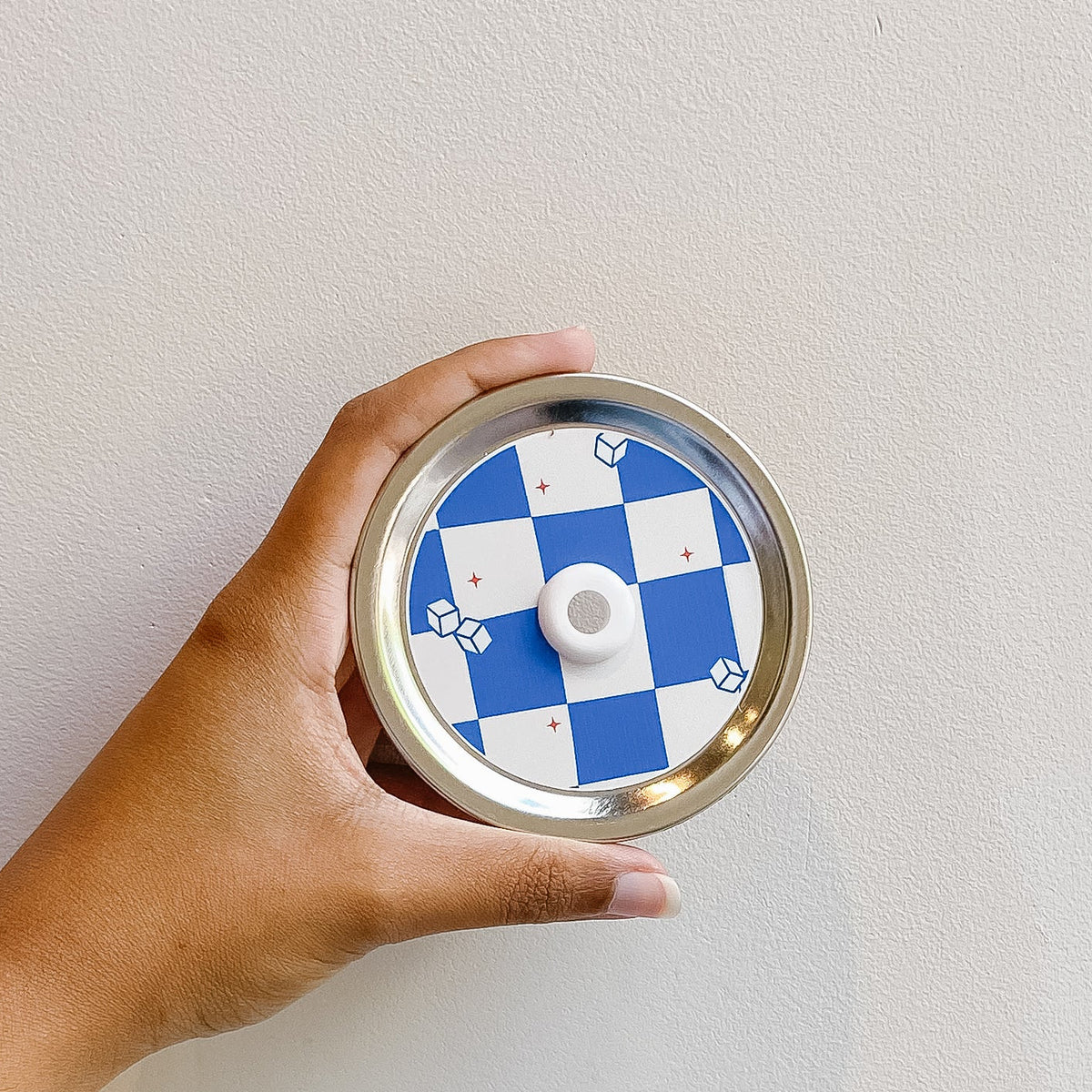 Hand holding mason jar patterned straw lid that has blue and white checkered design with small ice cube and red stars around 