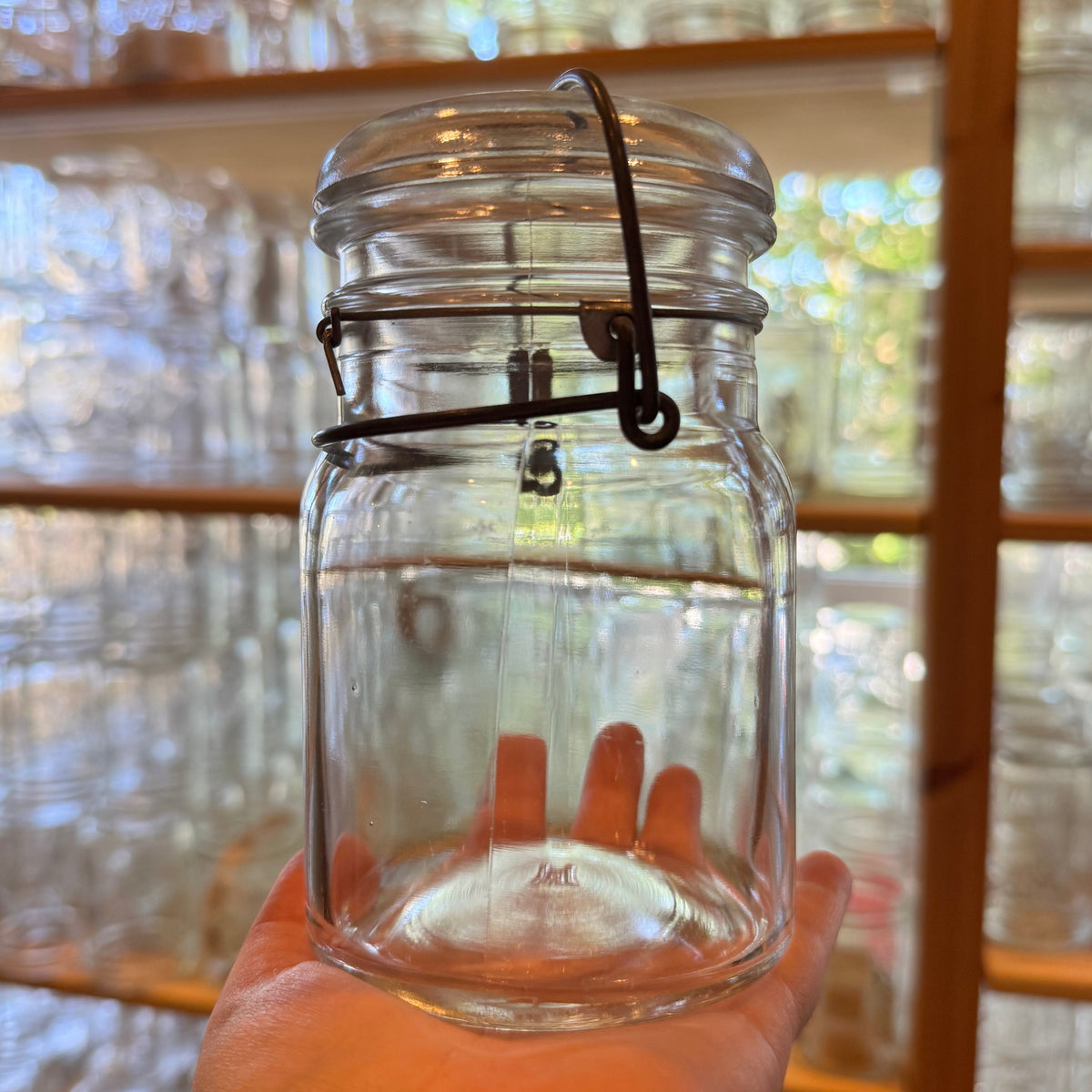 Hand holding a vintage 1920s unmarked Hazel Atlas wire bail pint mason jar with beaded neck, in store