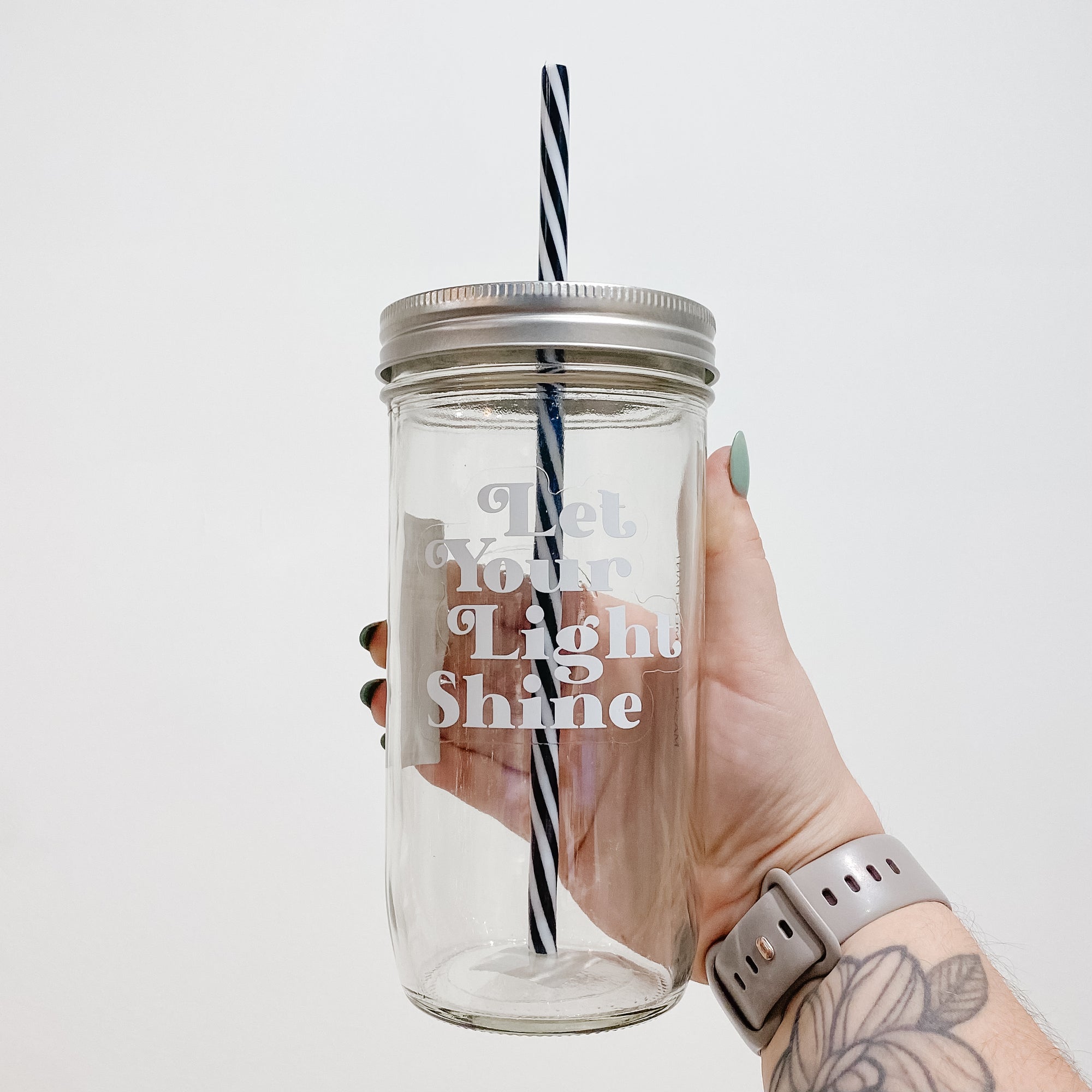 Mason jar tumbler that says “let your light shine” in white letters on a clear background