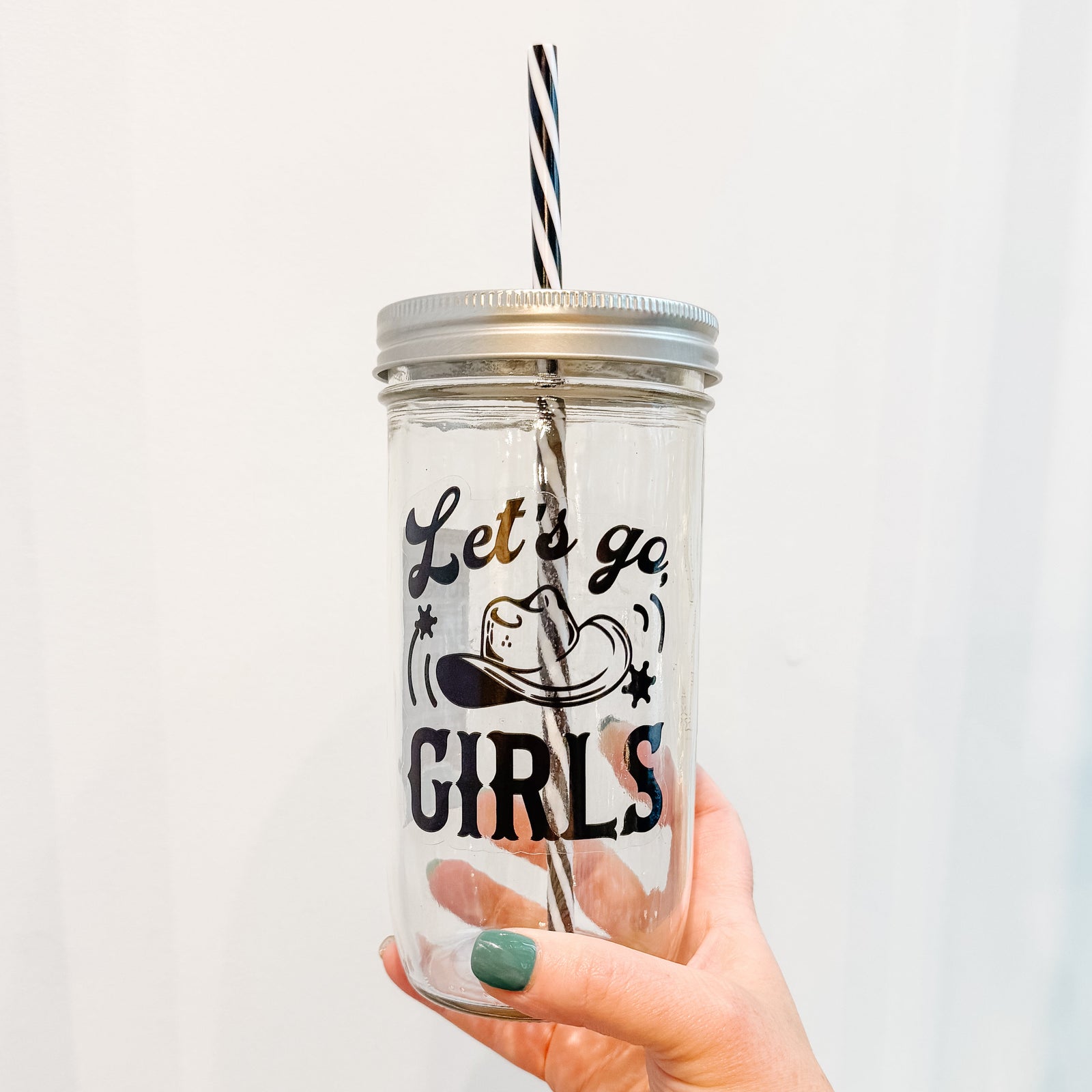 Hand holding a mason jar tumbler that reads lets go girls in black text on clear background with a cowboy hat in middle of print