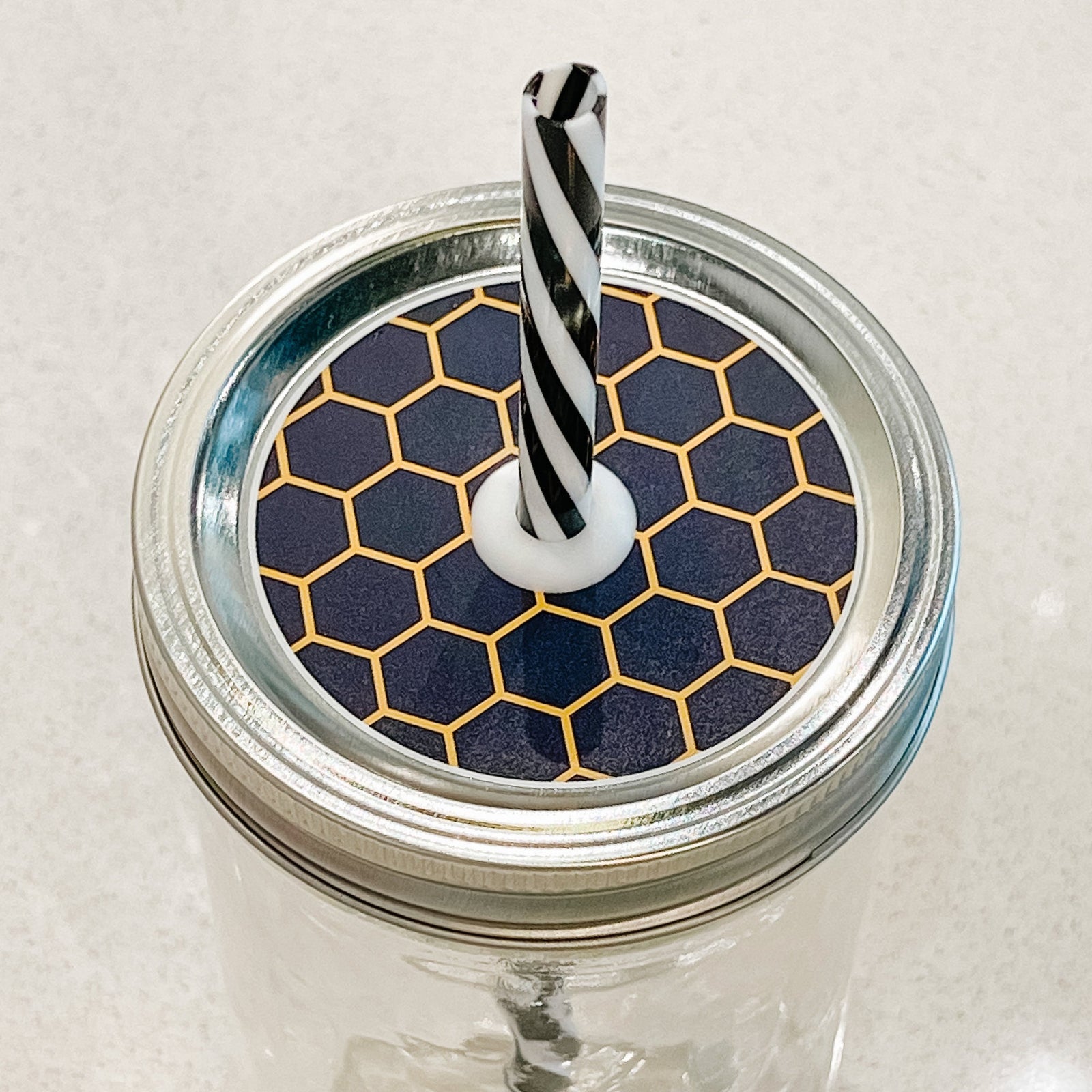 Hand holding mason jar straw lid that is a black and yellow honeycomb design