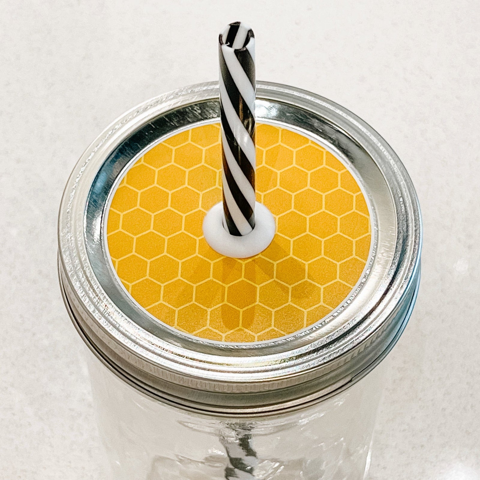 Hand holding mason jar patterned straw lid that is a yellow and orange honeycomb design
