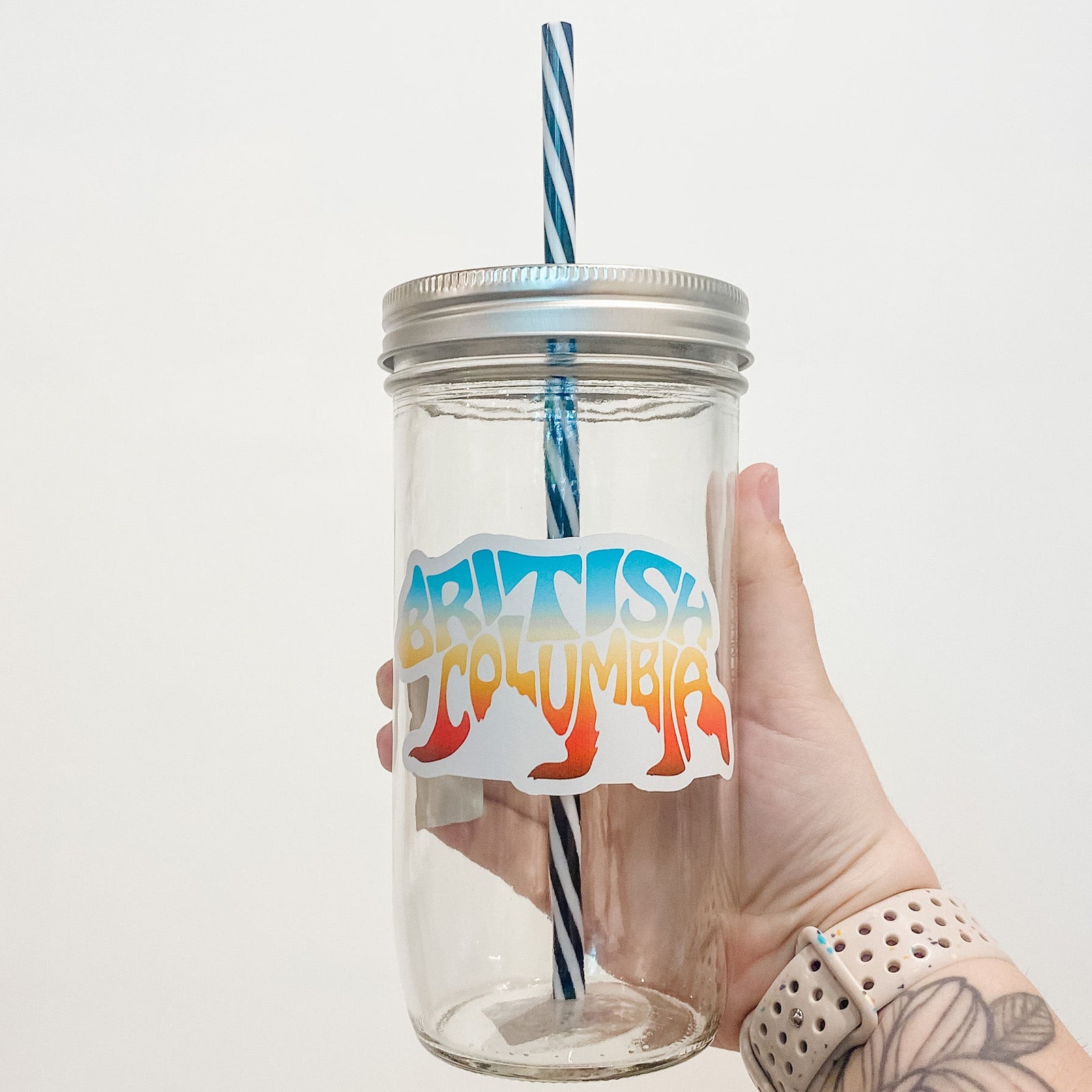 Hand holding mason jar that reads British Columbia in shape of bear. Colours are bright sunset gradient