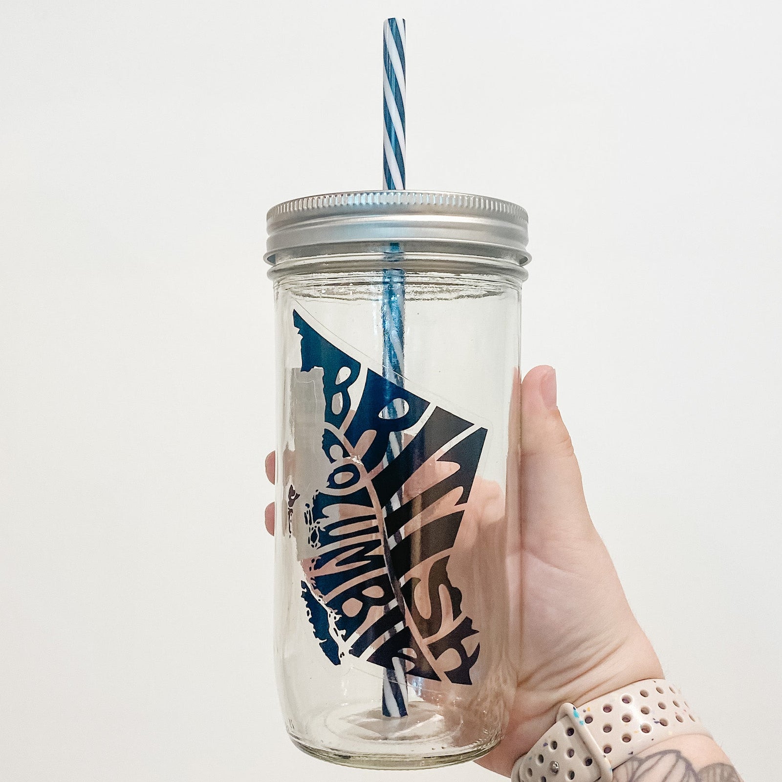 Hand holding mason jar that reads British Columbia in shape of province in black text and clear background.