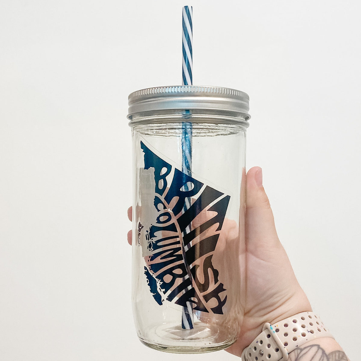 Hand holding mason jar that reads British Columbia in shape of province in black text and clear background.