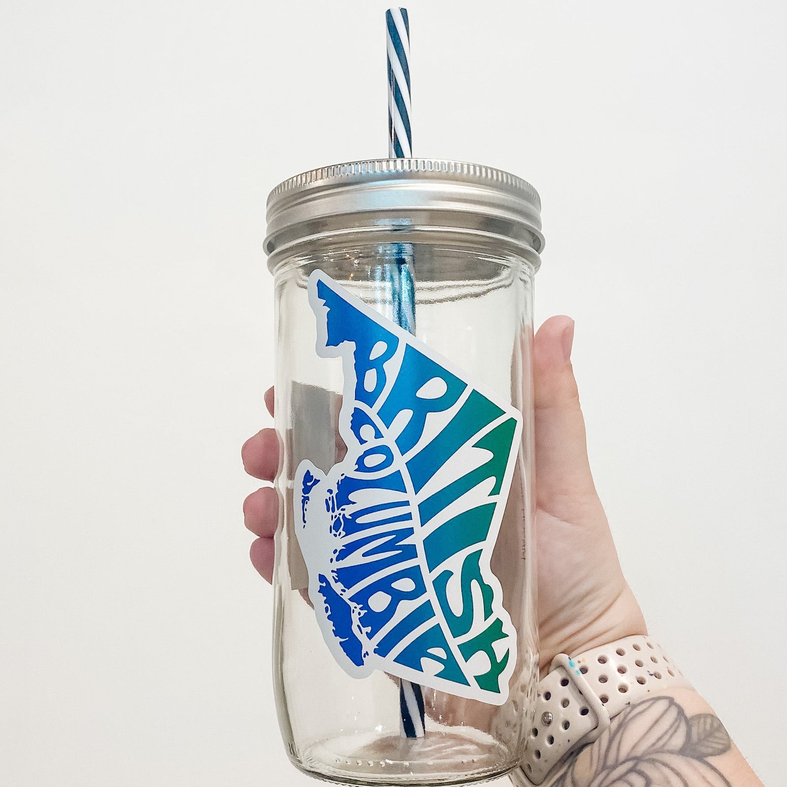 Hand holding mason jar that reads British Columbia in the shape of the province. Colours are blue and green ombré. 