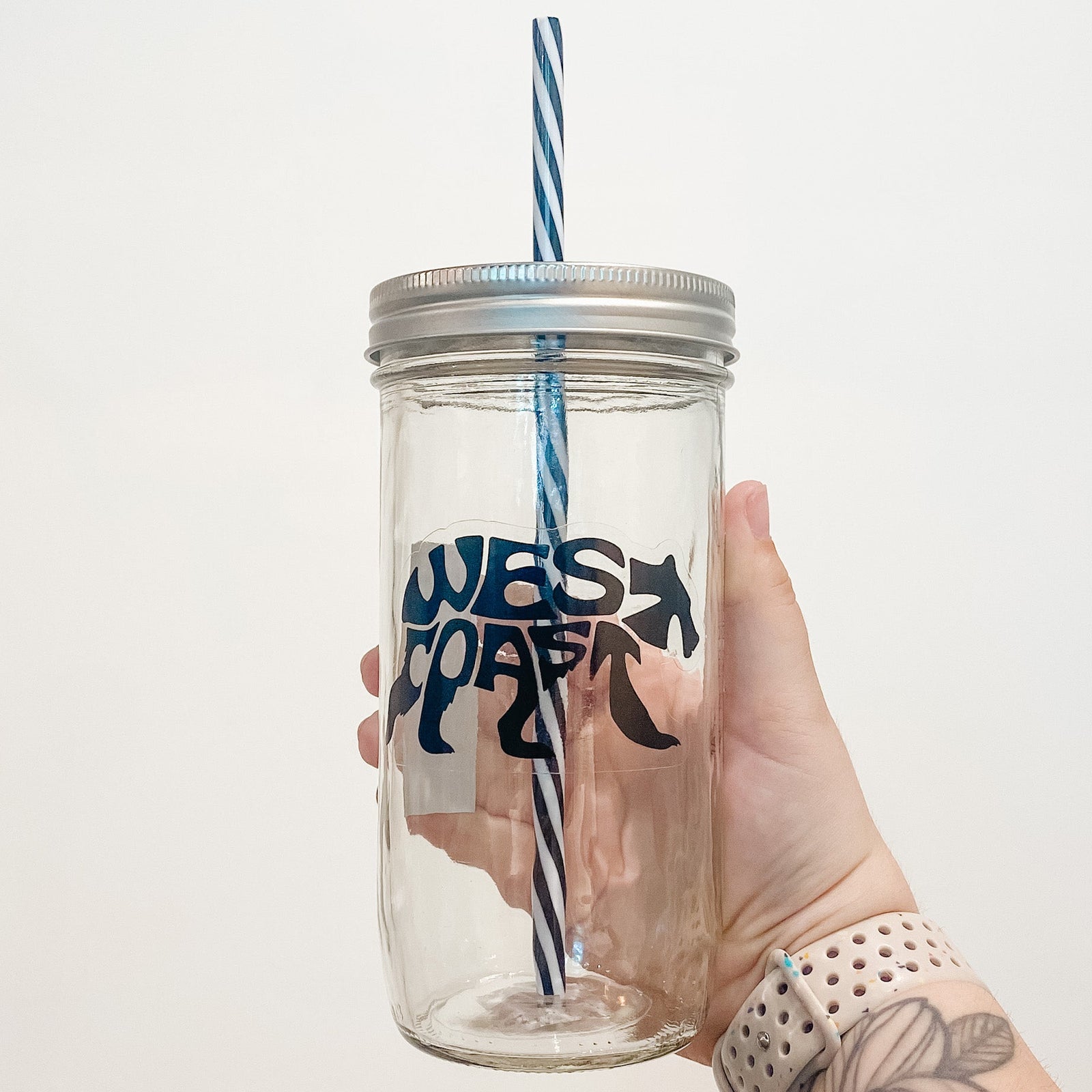 Hand holding mason jar that reads west coast in black text and shape of bear with clear background. 