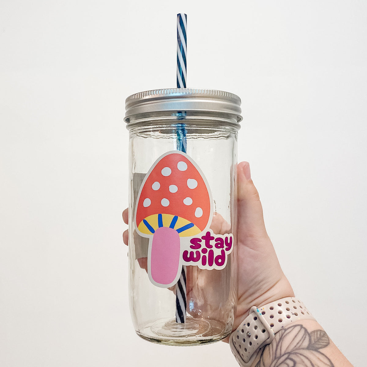 Hand holding a mason jar that reads stay wild with a colourful mushroom.