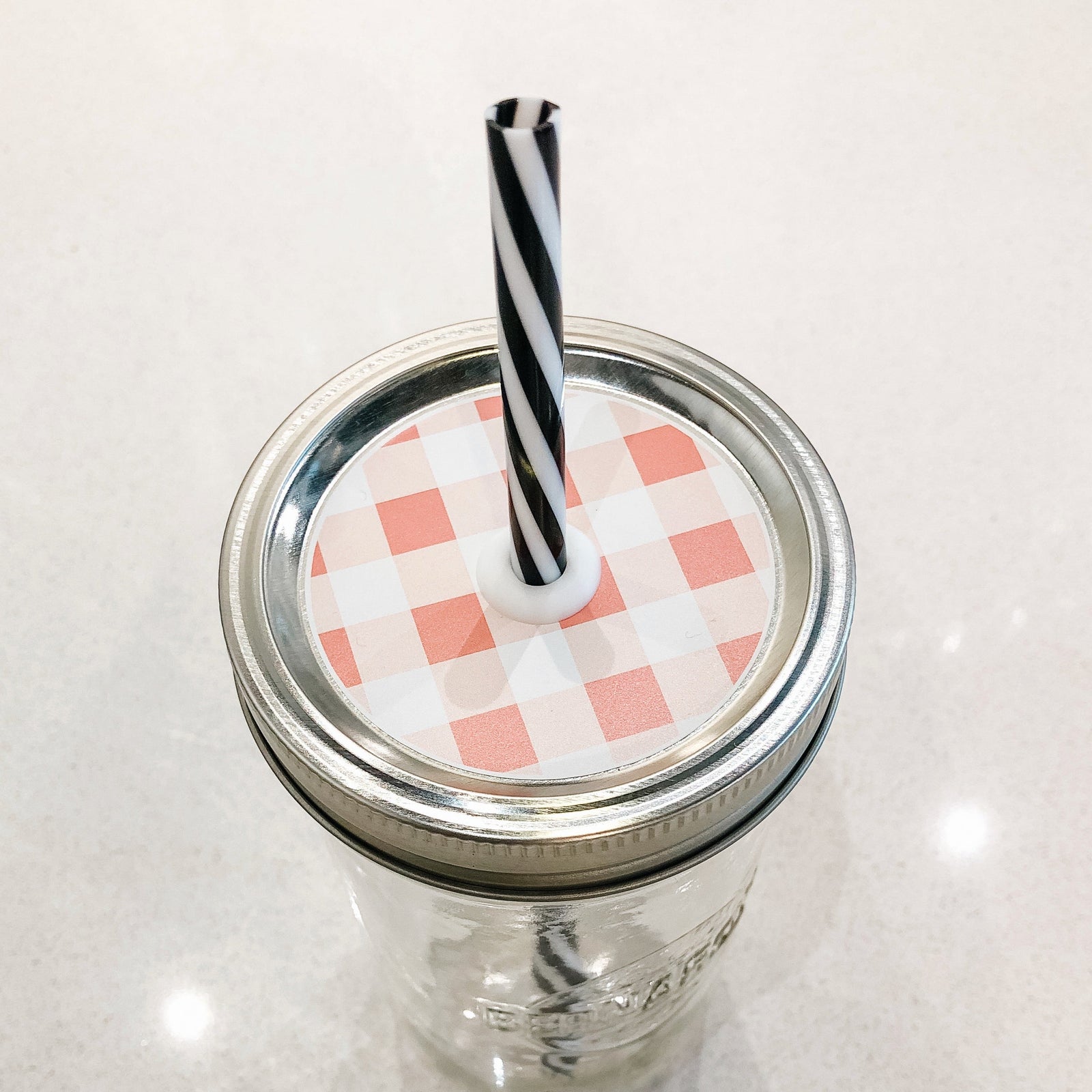 Hand holding mason jar straw lid with large white and peach gingham design
