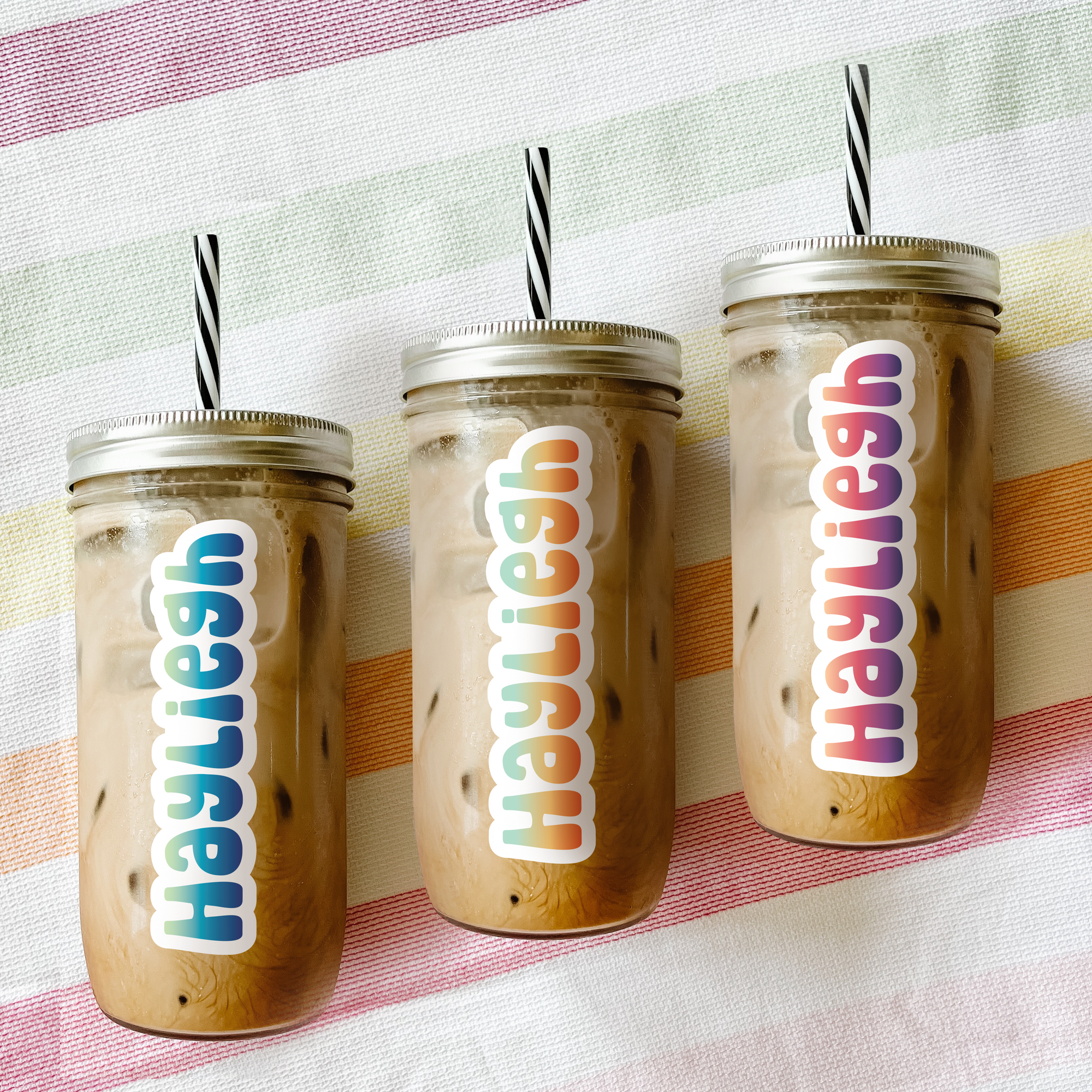 Three custom tumblers filled with iced coffee laying on a colourful beach towel.