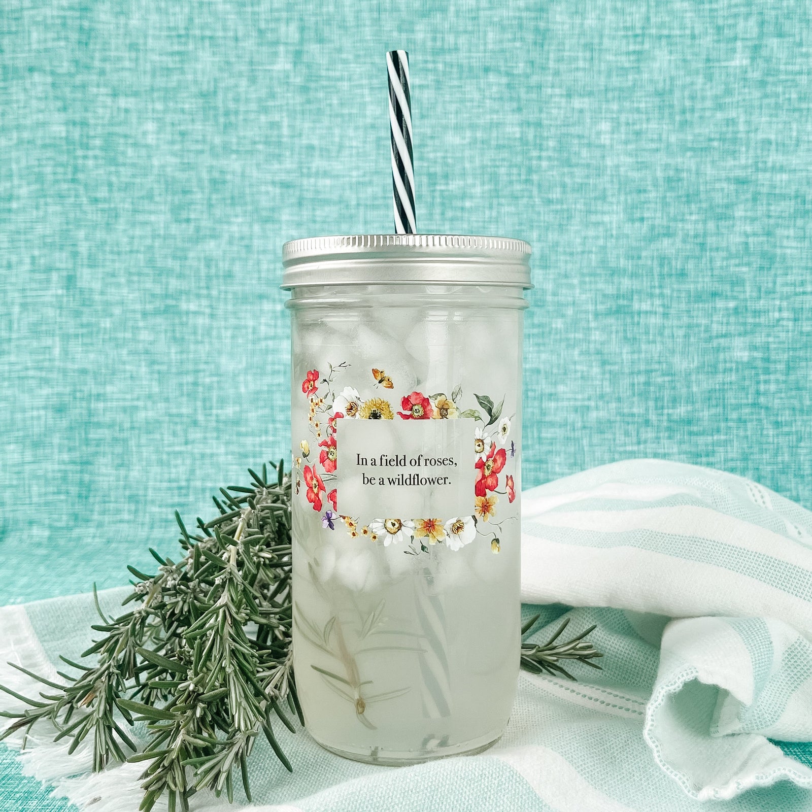 Mason jar tumbler that says “In a field of roses, be a wildflower” with flowers creating a rectangle around the phrase