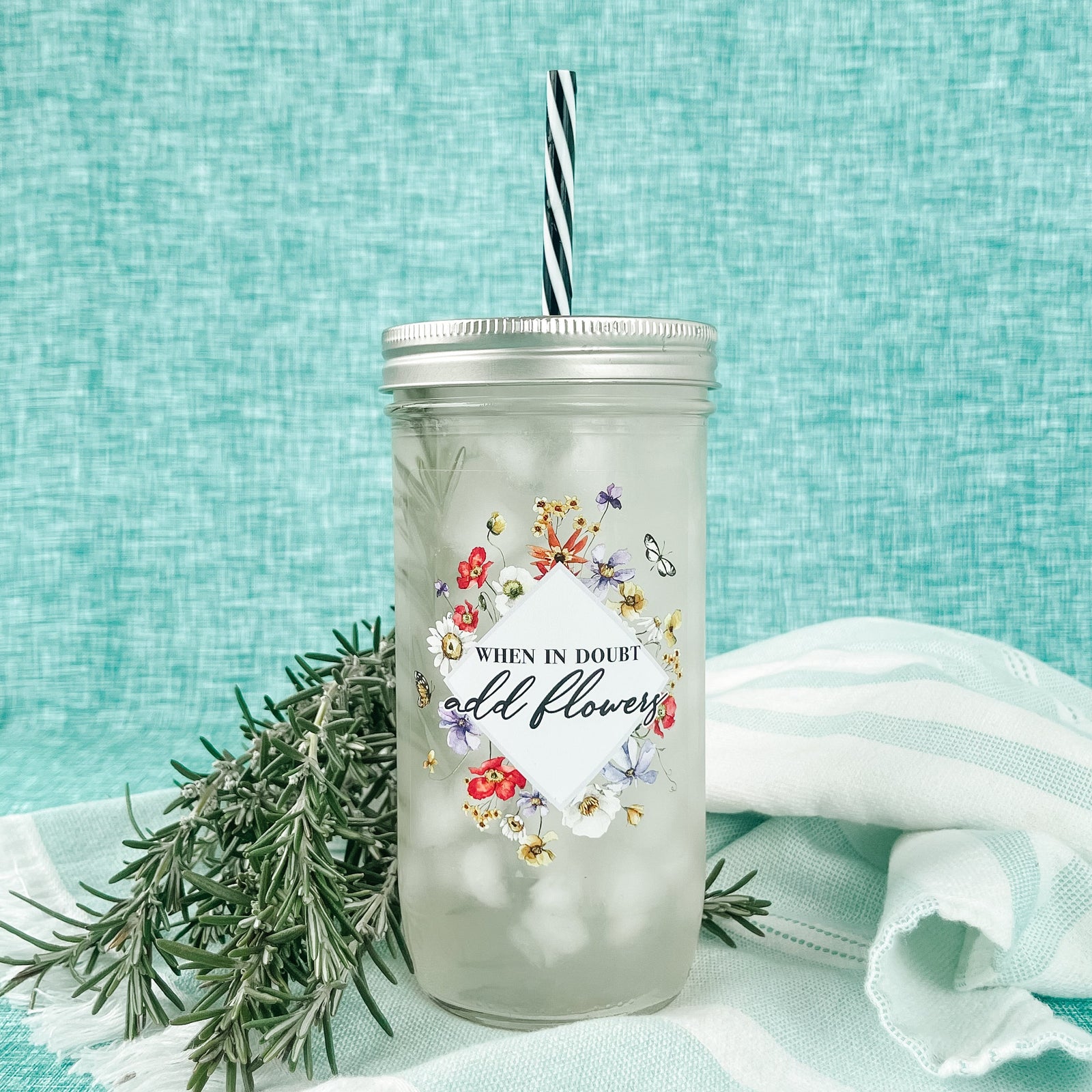 Mason jar tumbler that says “when in doubt add flowers” with flowers creating a diamond around the words.