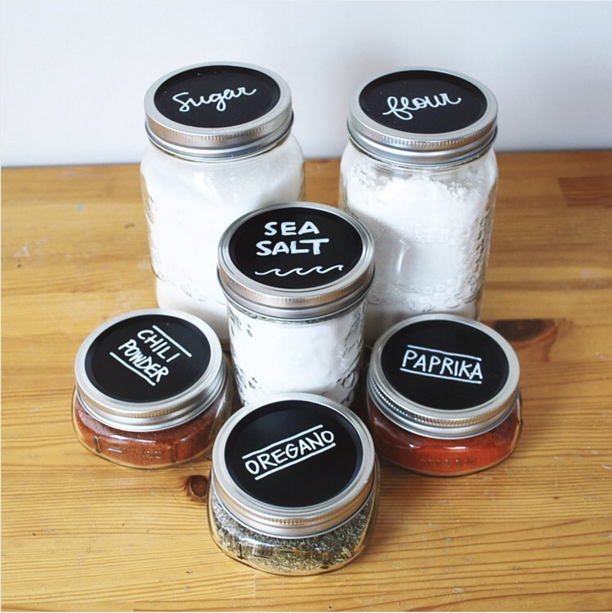 6 various wide mouth mason jars with MasonTops Chalkboard lids on top. Various pantry ingredients are in the jars and the lid label reflects the ingredients.