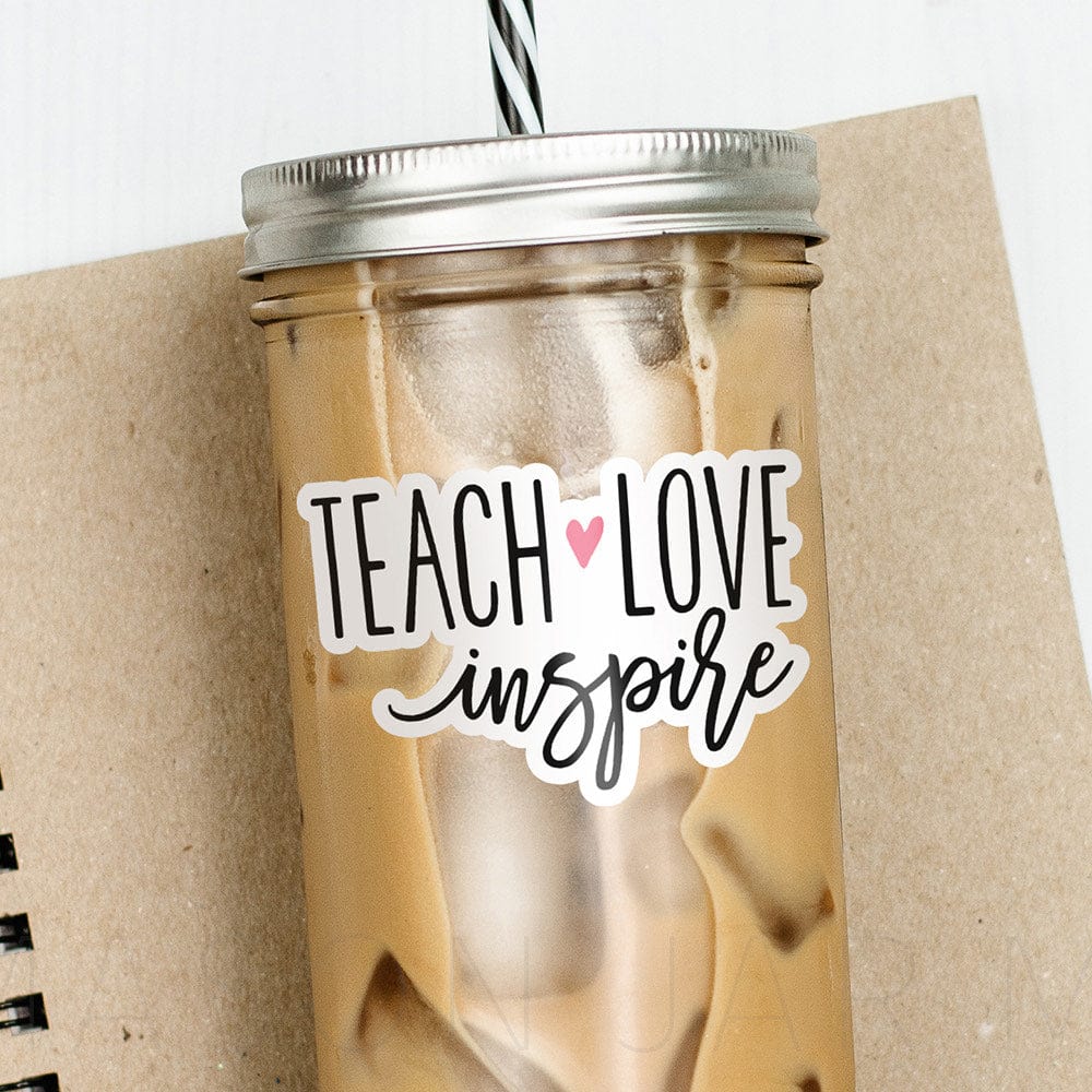 Tumbler with iced coffee and print that says "Tech Love Inspire" with a heart design in text. Photographed against a neutral colored notebook and some color pencils.