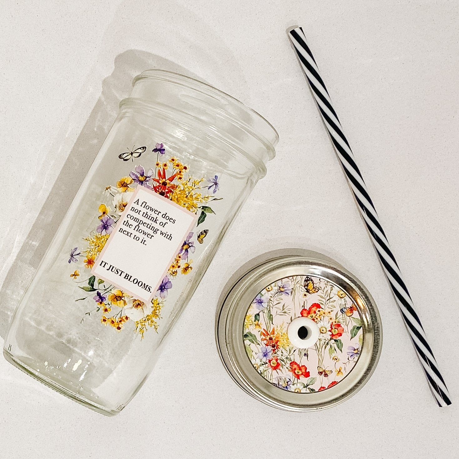 Mason jar tumbler that says “A flower does not think of competing with the flower next to it. It just blooms.” With flowers creating a rectangle around the words.