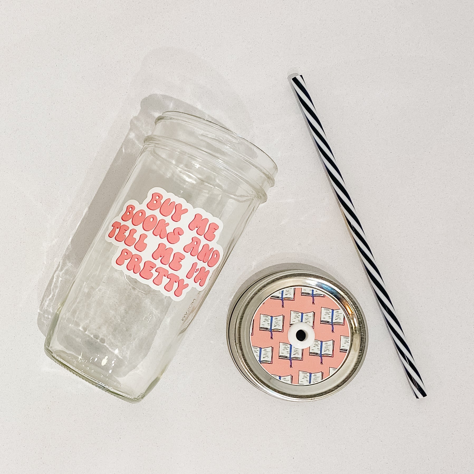 Mason jar tumbler that says “buy me books and tell me I’m pretty” in pink bubble letters on a white background.