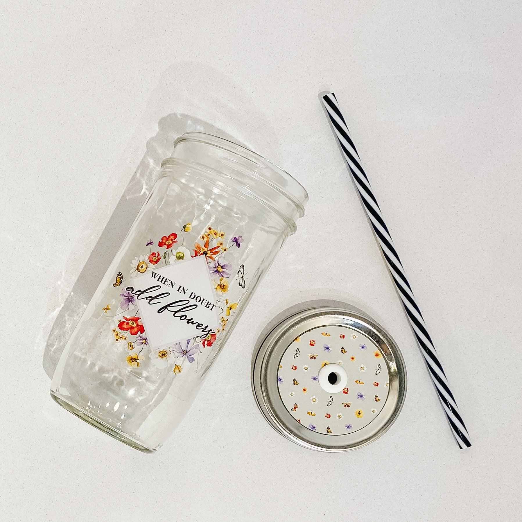 Mason jar tumbler that says “when in doubt add flowers” with flowers creating a diamond around the words.