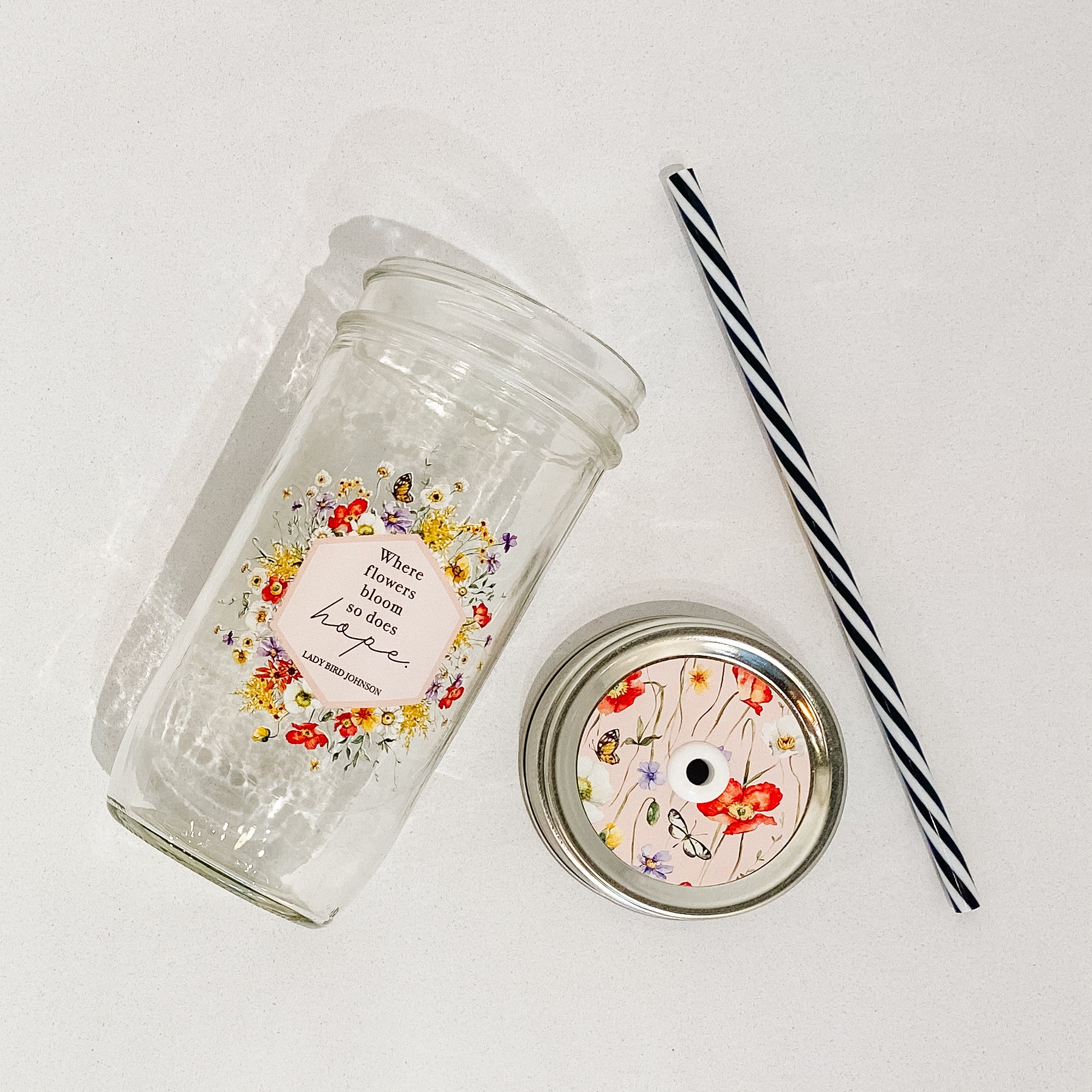 Mason jar tumbler that says “Where flowers bloom so does hope. Lady Bird Johnson” with flowers and butterflies creating a hexagon around the quote.