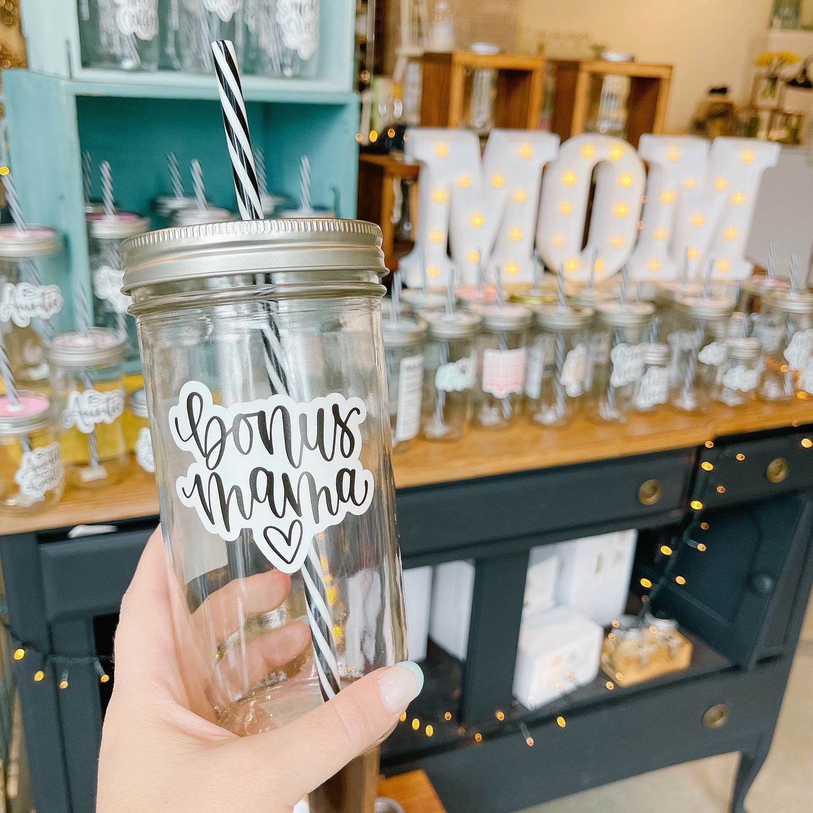 Hand holding a mason jar tumbler that says “bonus mama” with a heart underneath. 