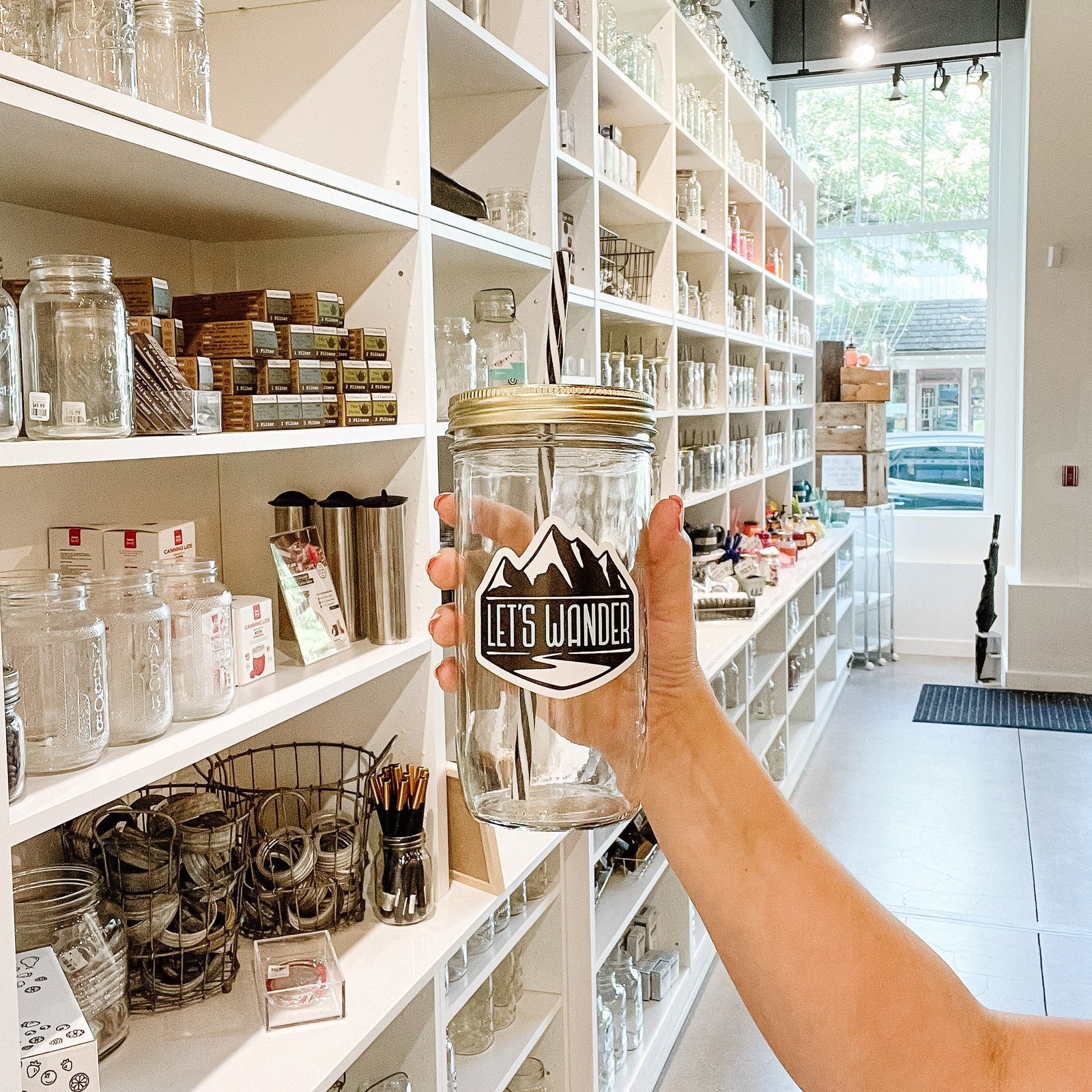 Hand holding a mason jar tumbler that says “let’s wander” with mountains behind the words.