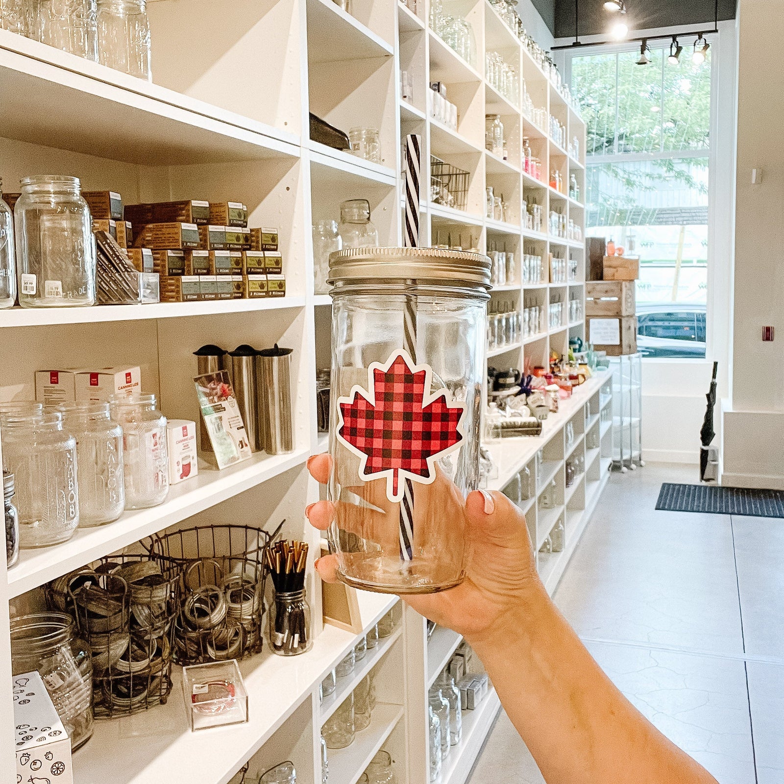 Hand holding a mason jar tumbler that has a maple leaf on it in a black and red plaid pattern. 