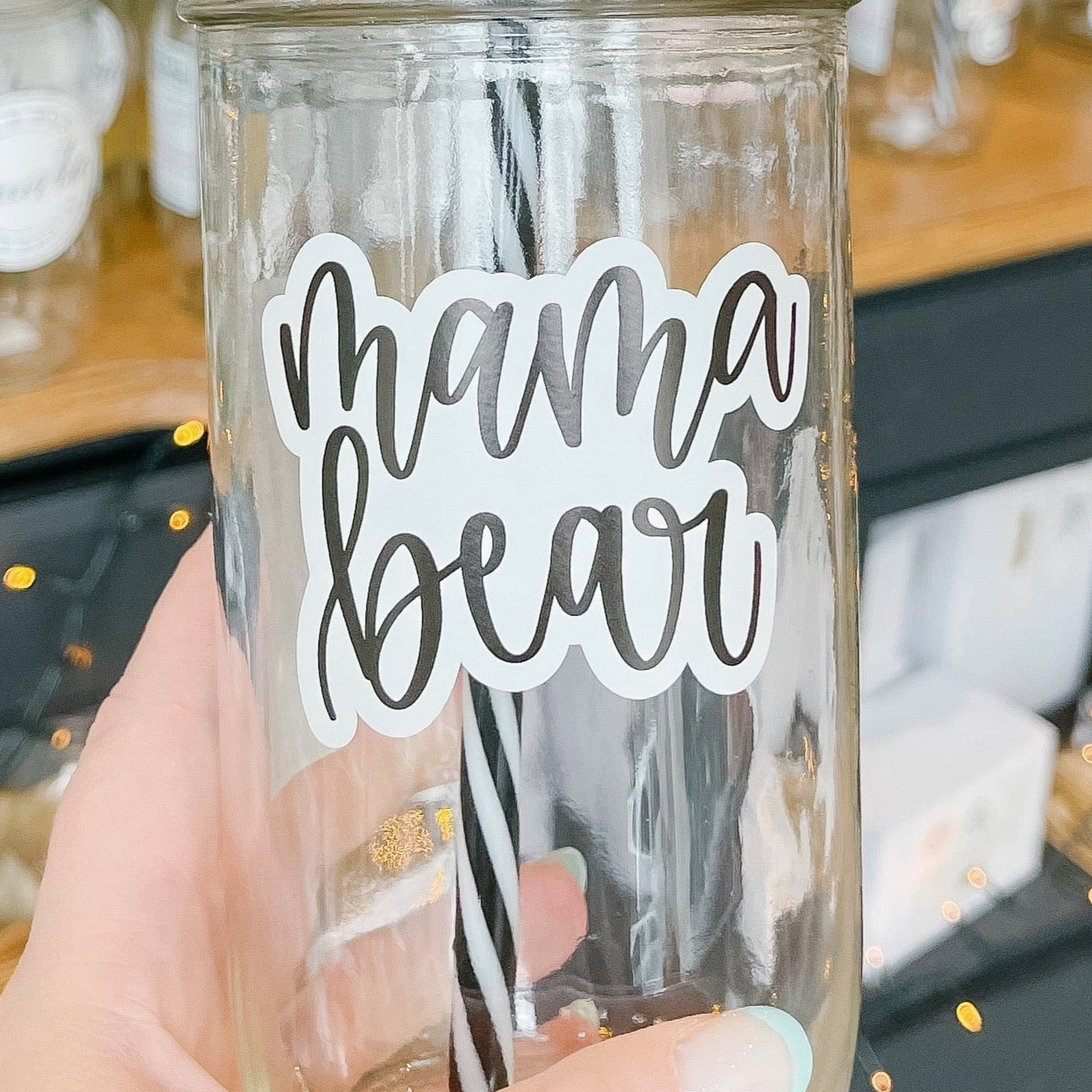 Hand holding a mason jar tumbler that says "mama bear” in black script on a white background