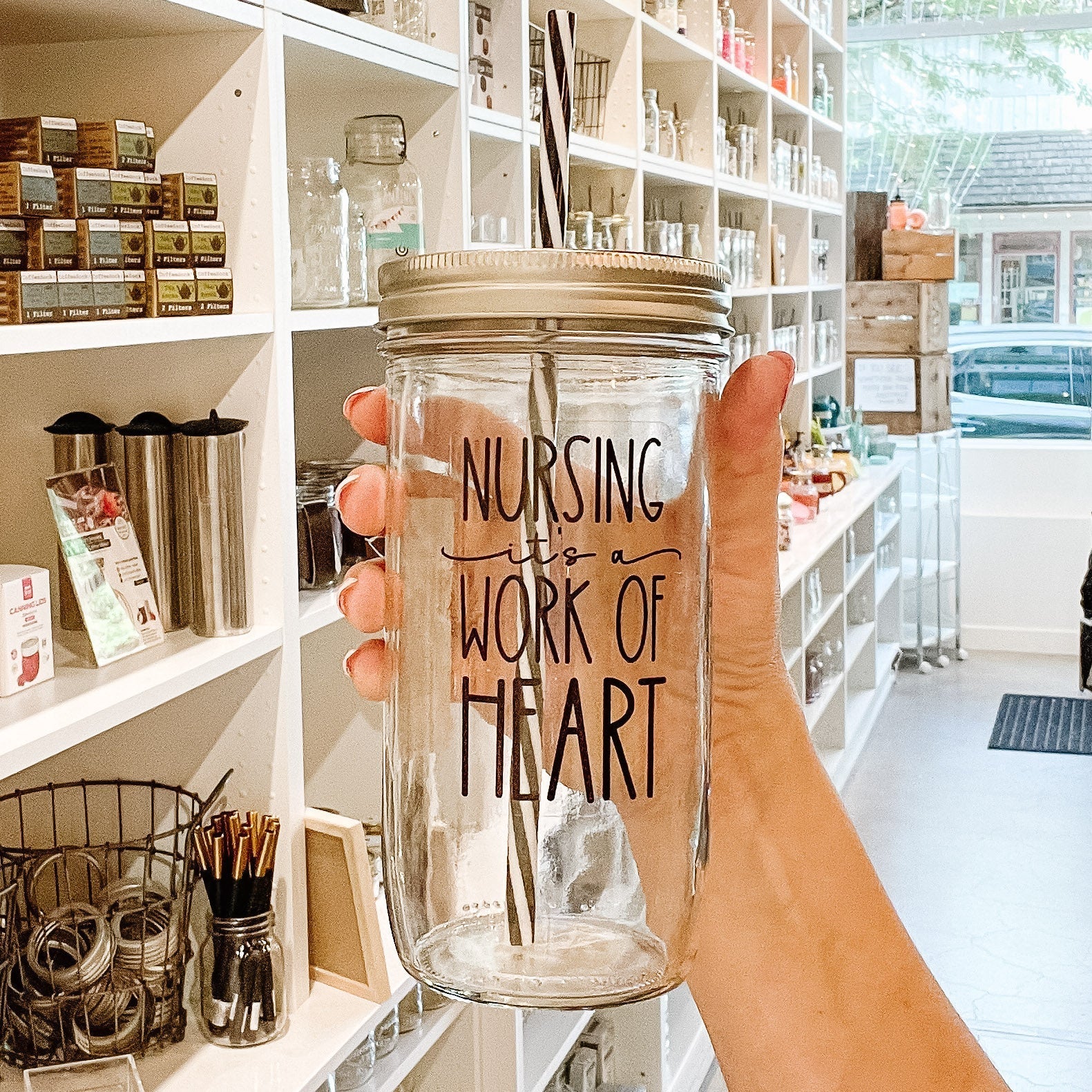 Hand holding a mason jar tumbler that says “nursing it’s a work of heart”