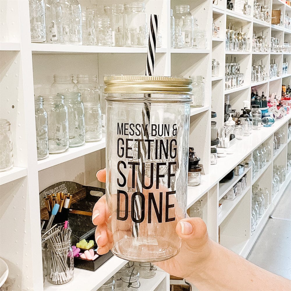 A photo of a mason jar tumbler with a sticker text that says " Messy Bun & Getting Stuff Done" drinking jar