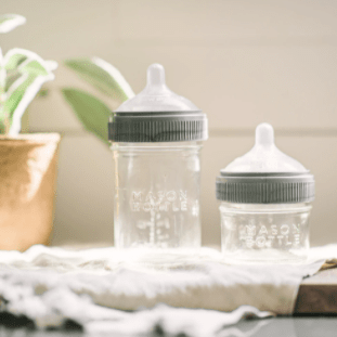 Photo of 8oz and 4oz mason bottles set in a table cloth in a cutting board on a countertop with a potted plant beside the bottles.