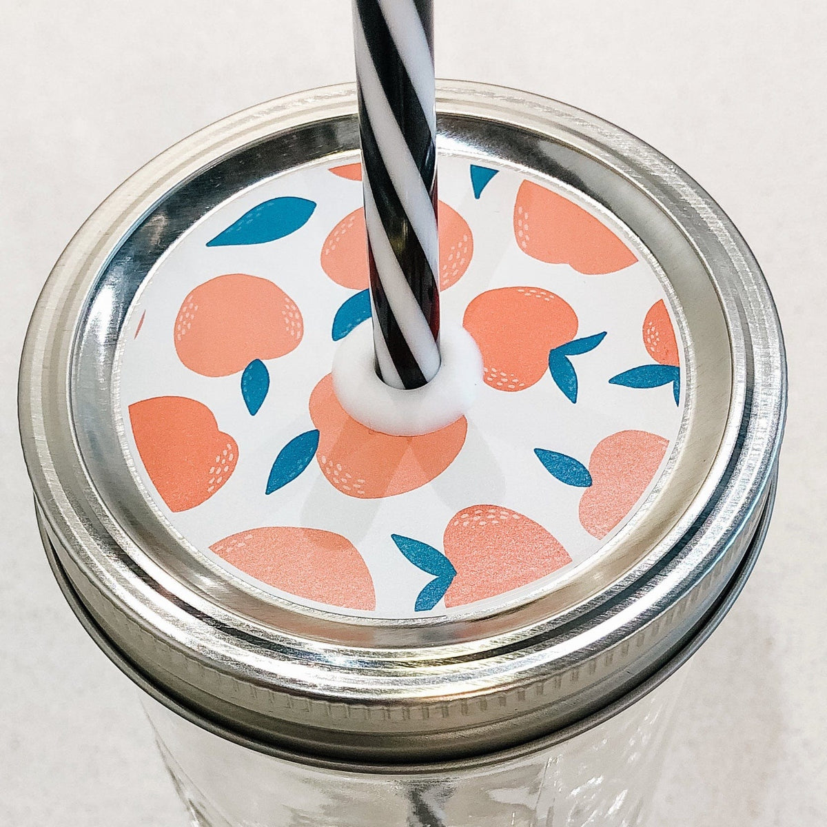 Close up photo of mason jar straw lid with peaches on print. 