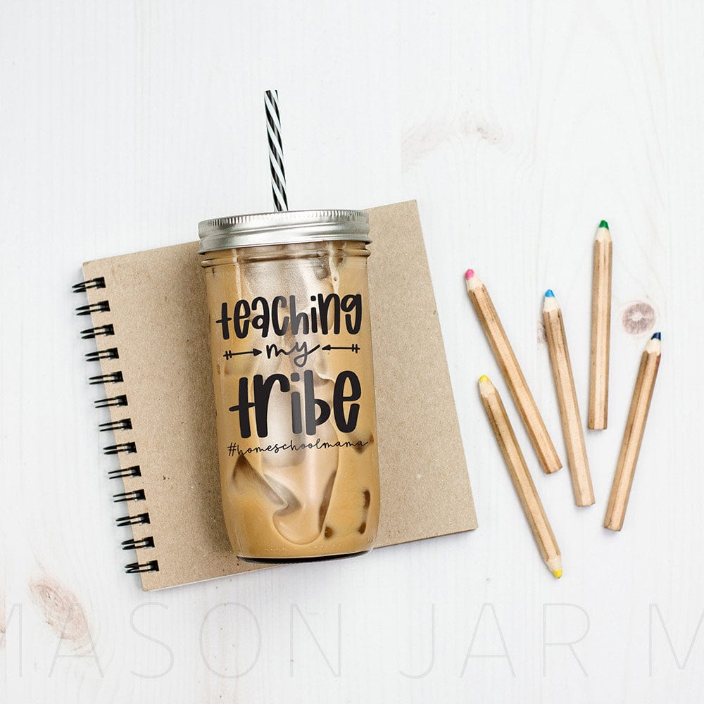 &quot;Teaching My Tribe&quot; print on tumbler with iced coffee and #homeschoolmama against a neutral colored notebook and some color pencils.