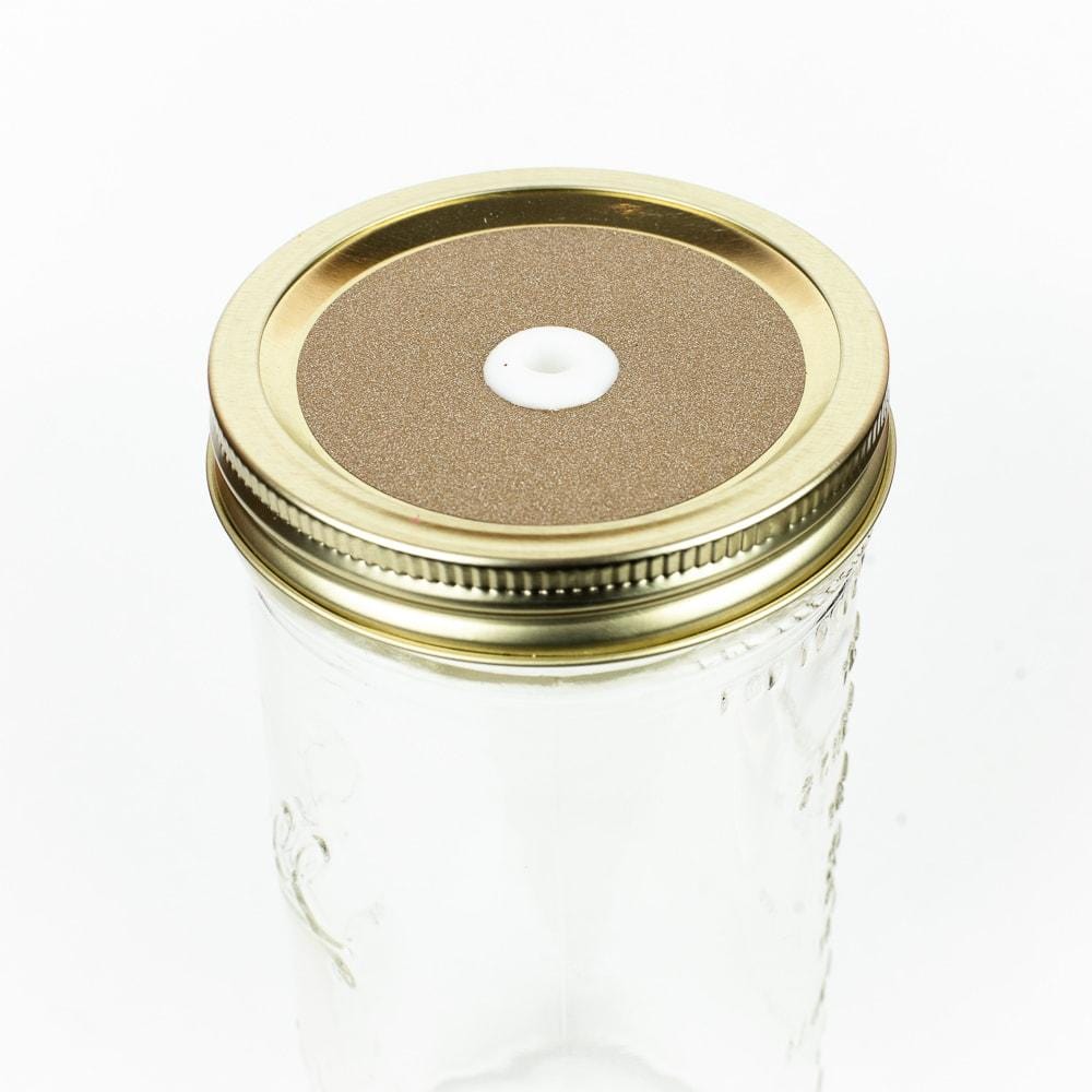 Gold Glitter Mason Jar Straw Lid on a golden lid against a white background.