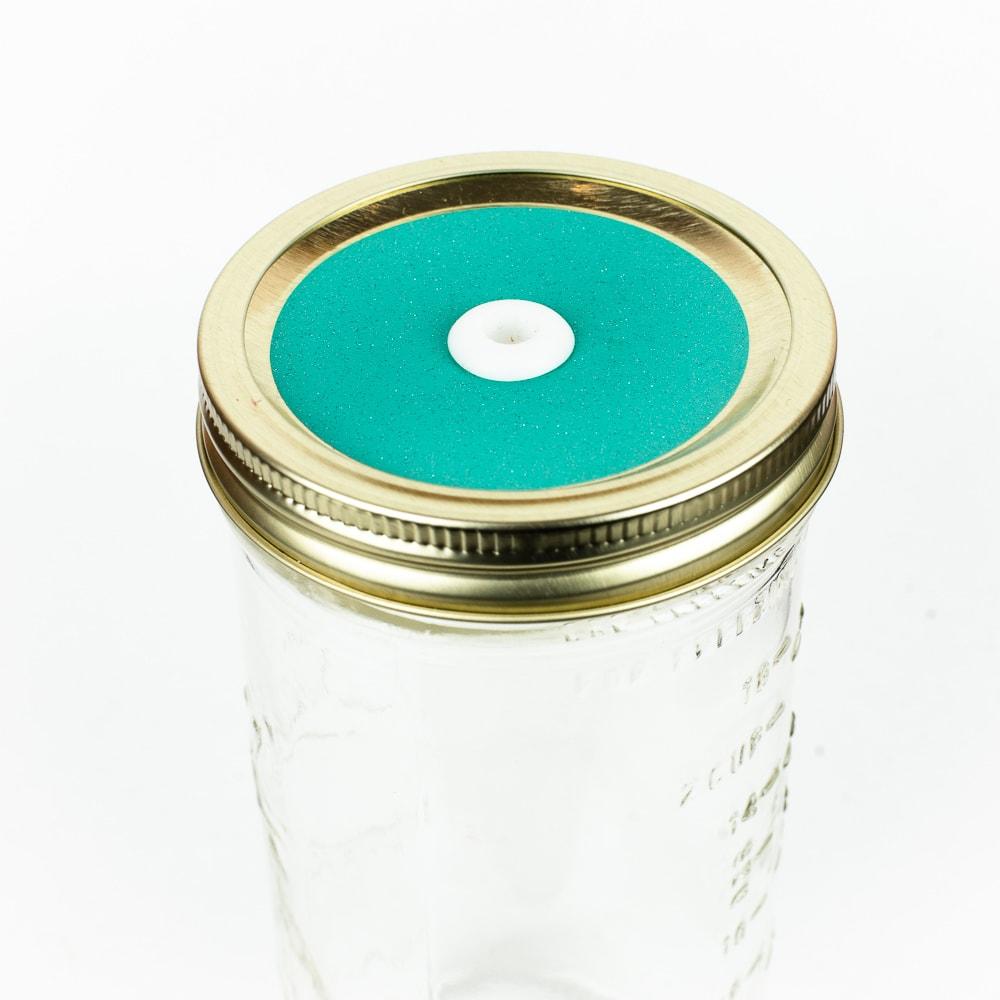 Bright teal Glitter Mason Jar Straw Lid on a golden lid against a white background.