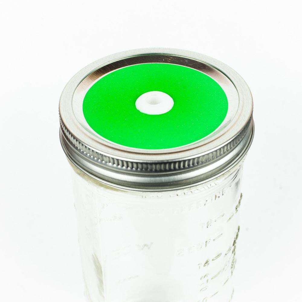 Hot green Glitter Mason Jar Straw Lid on a silver lid against a white background.