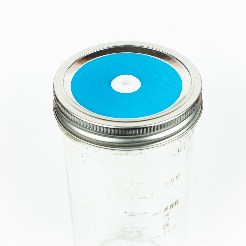 Bright blue Glitter Mason Jar Straw Lid on a silver lid against a white background.