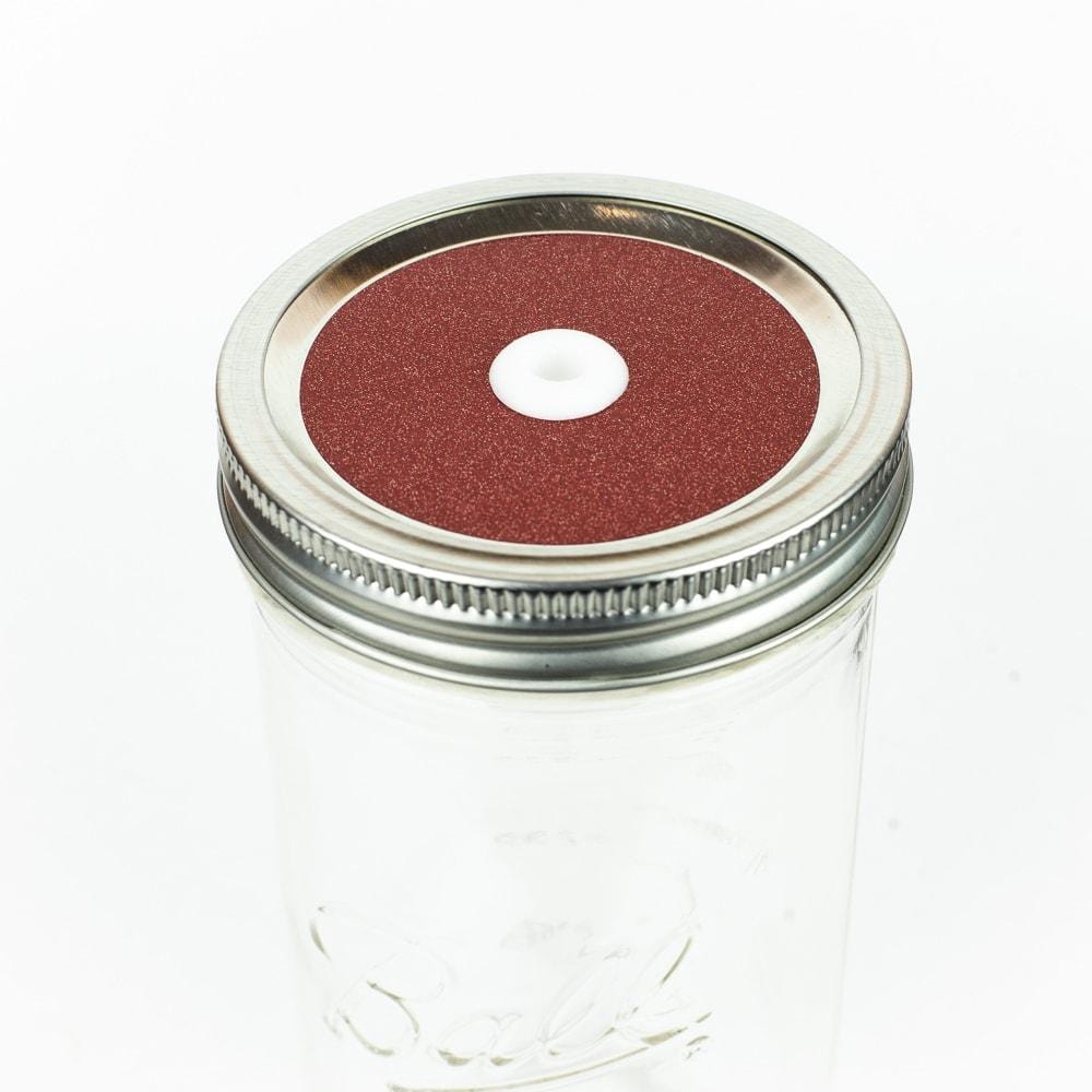 Orangey red Glitter Mason Jar Straw Lid on a silver lid against a white background.