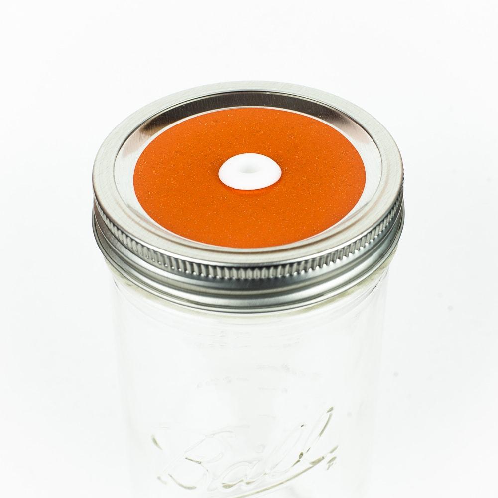 Tangerine orange Glitter Mason Jar Straw Lid on a silver lid against a white background.