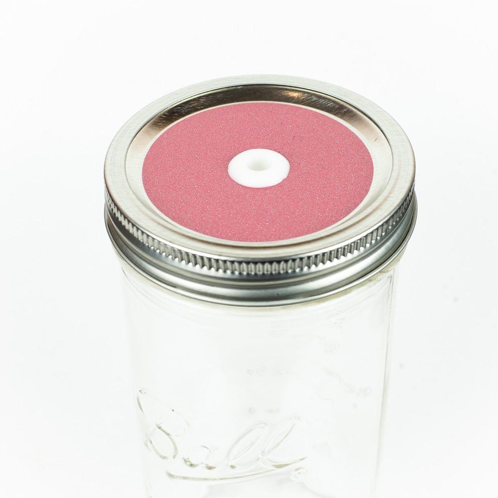 Salmon pink Glitter Mason Jar Straw Lid on a silver lid against a white background.
