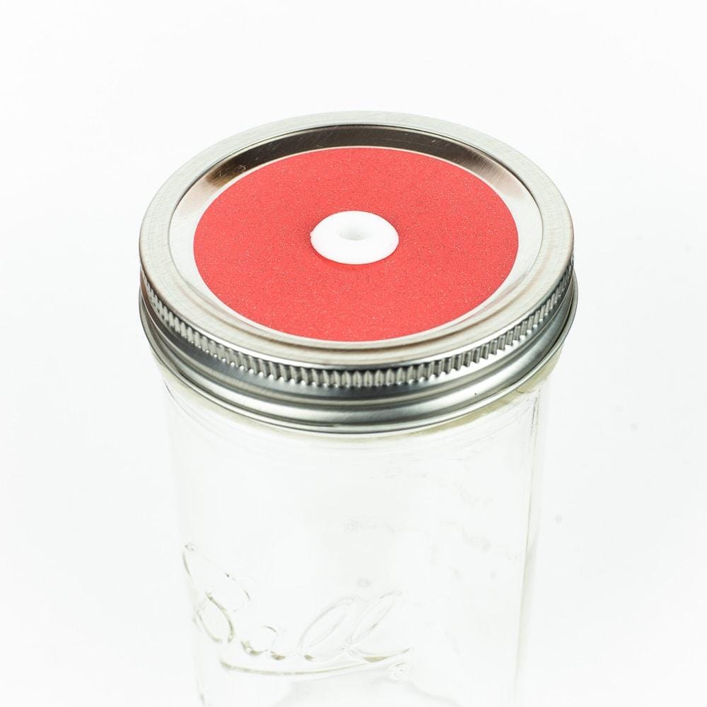 Coral red Glitter Mason Jar Straw Lid on a silver lid against a white background.