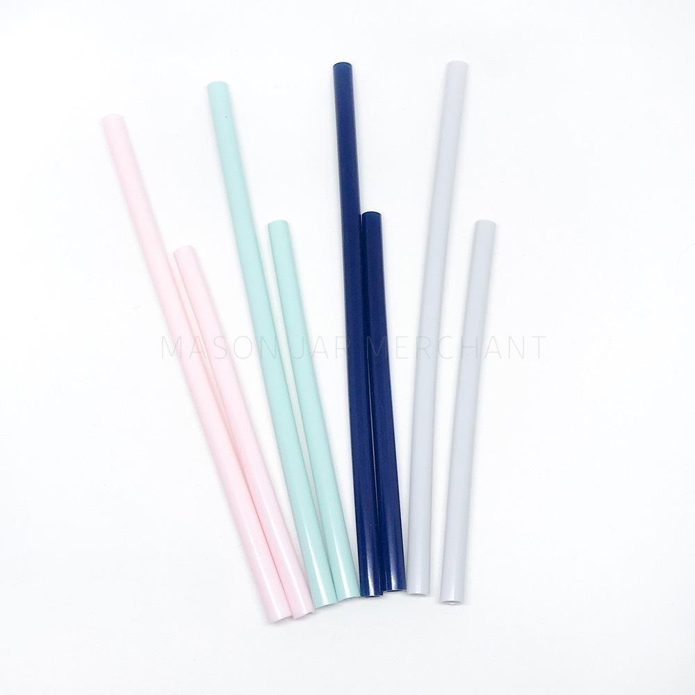 4 reusable silicone straws sit on a white background. Some short and some long, in pink, aqua, navy blue and white