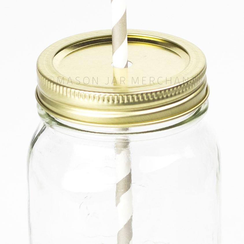 close up of a glass reusable mason jar with a gold straw lid and a grey and white stripped paper straw