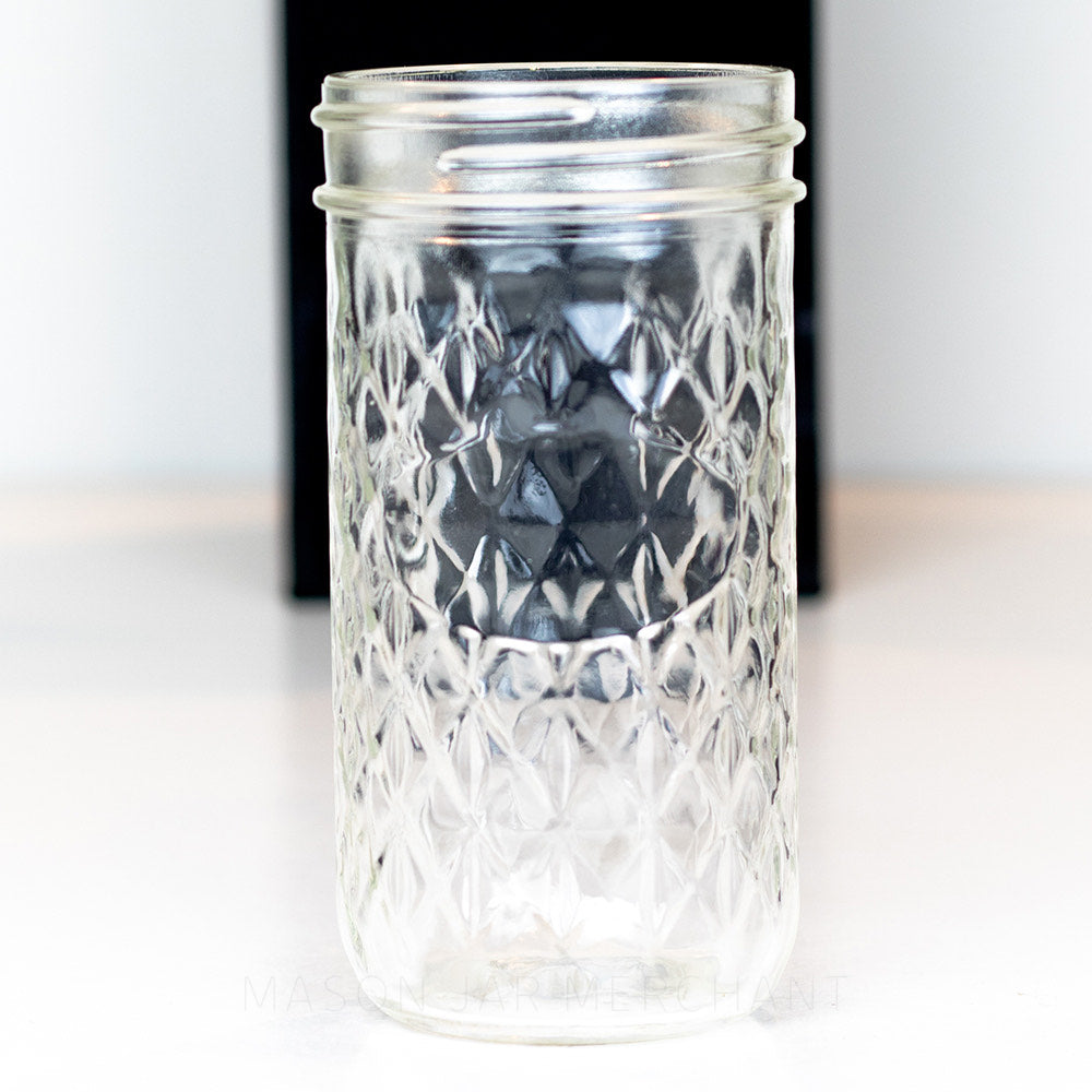 A close up of a Unique 10 oz regular mouth mason jar. Tall and thin with a quilted pattern all over except for space to add a label. On a white background
