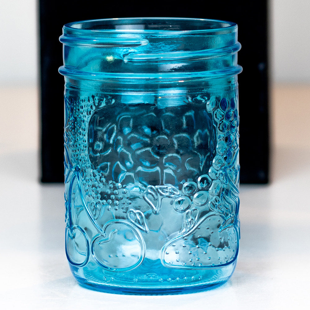 Fruity patterned blue regular mouth half pint mason jar against  a black backdrop