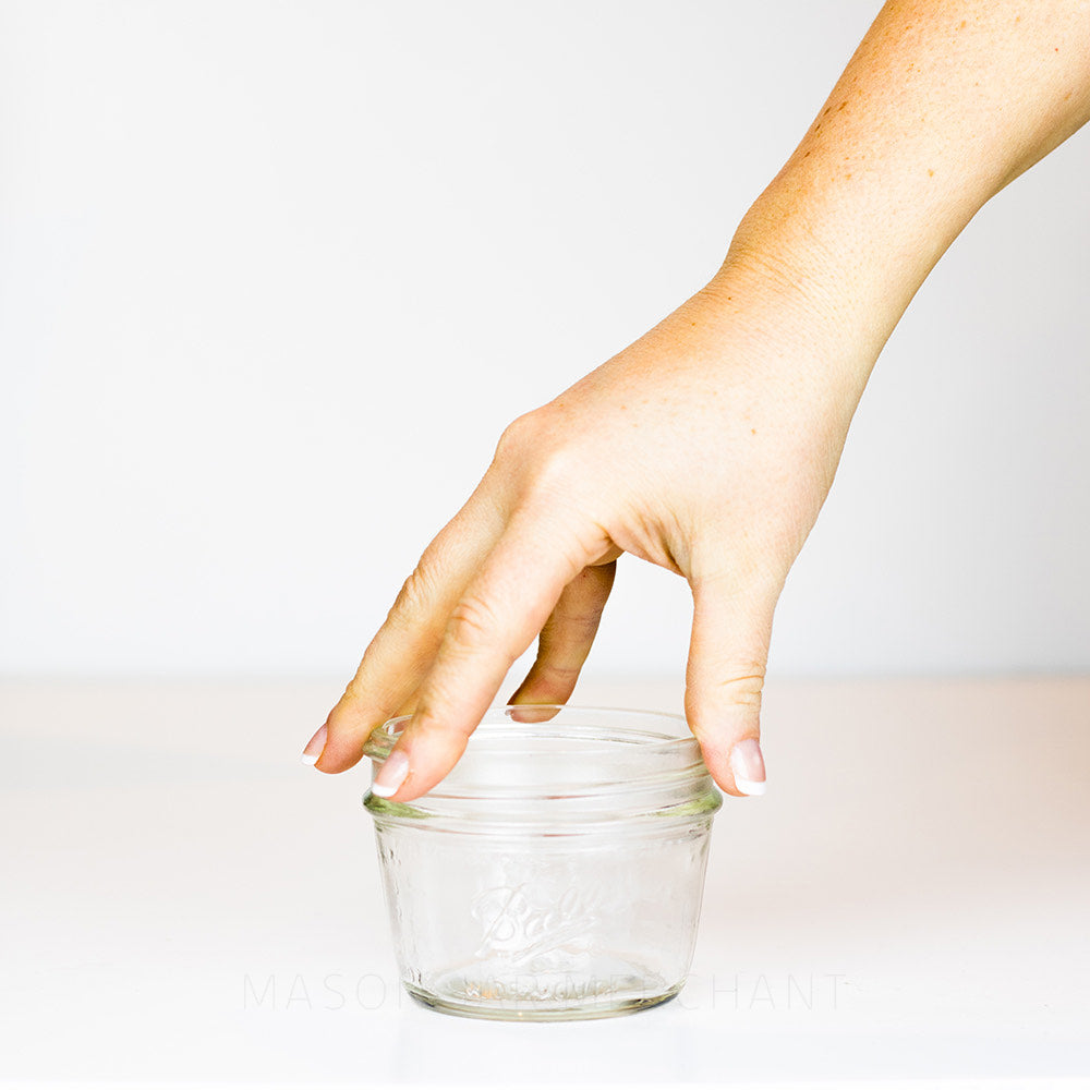 A ball wide mouth half pint mason jar against a white background with a hand holding it for size reference