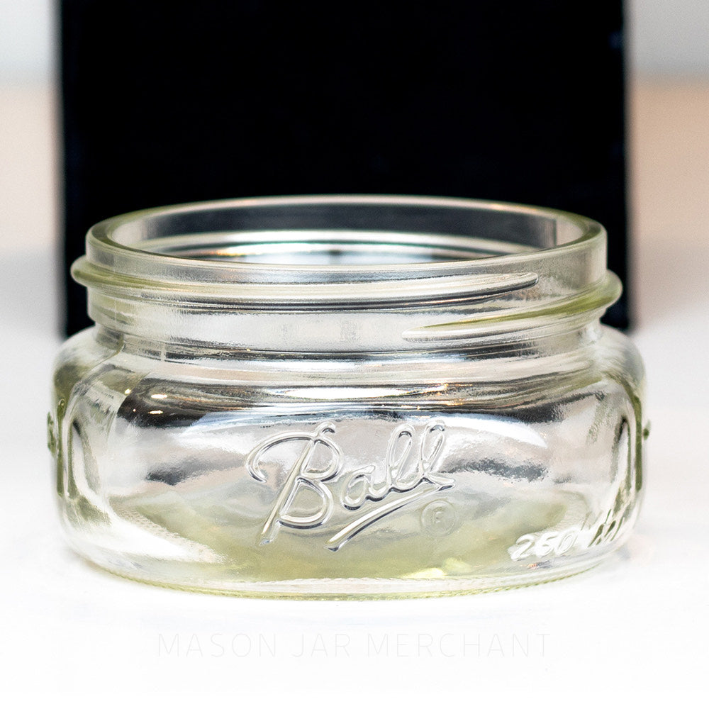 Close up of a Unique shallow wide mouth half pint mason jar with Ball logo against a white background