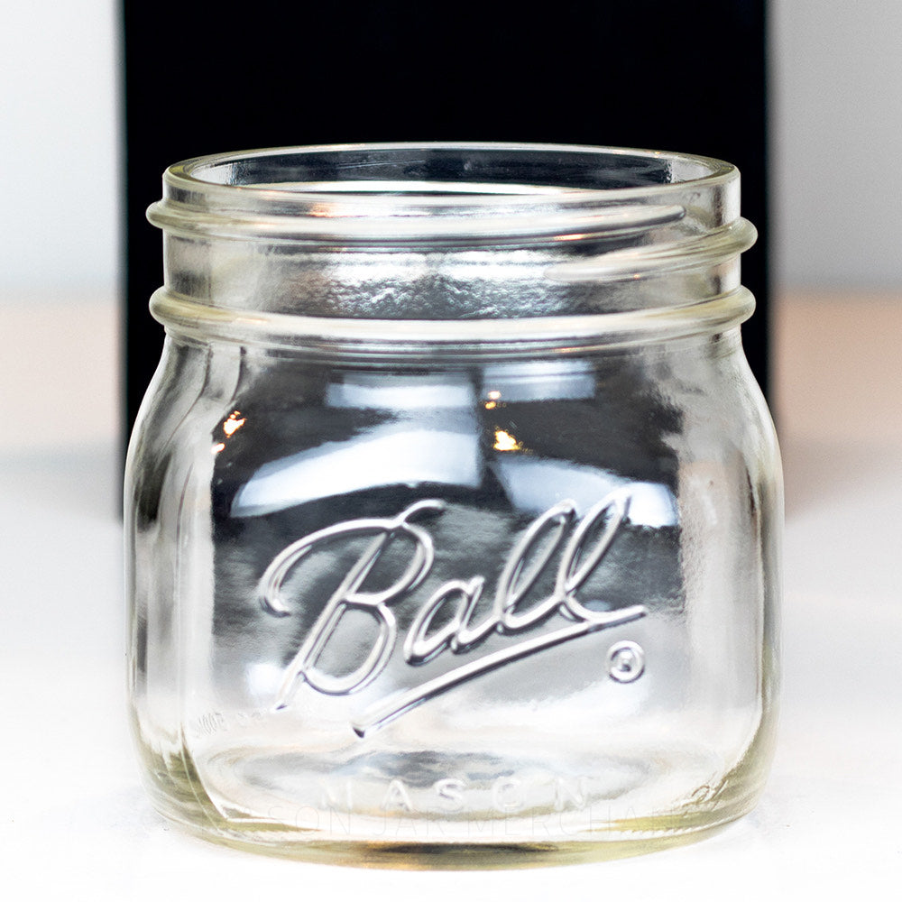 Close up of a Ball wide mouth pint mason jar with a short square body against a white background